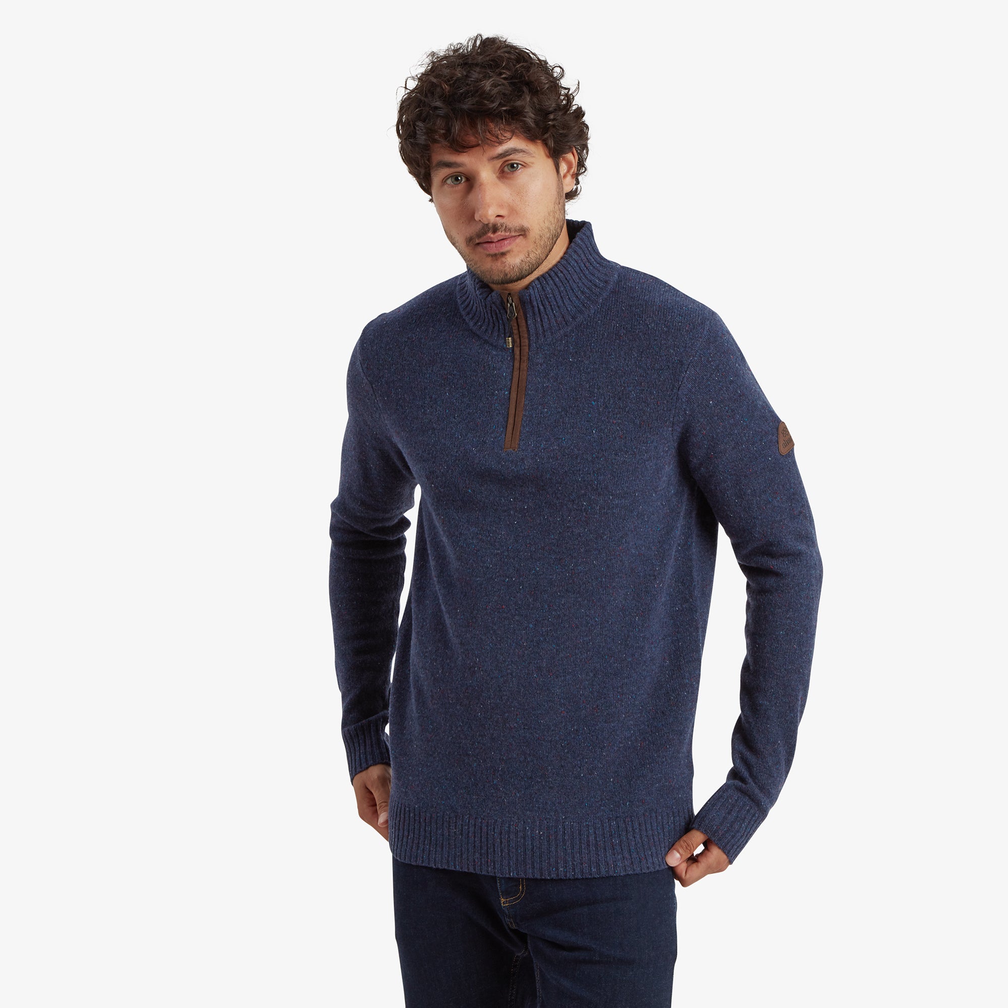 A man wears a stylish Sherpa Adventure Gear Kangtega Quarter Zip Sweater in Blue, paired with dark blue jeans. The sweater features a ribbed high neck with a brown suede zipper pull, adding a touch of sophistication.