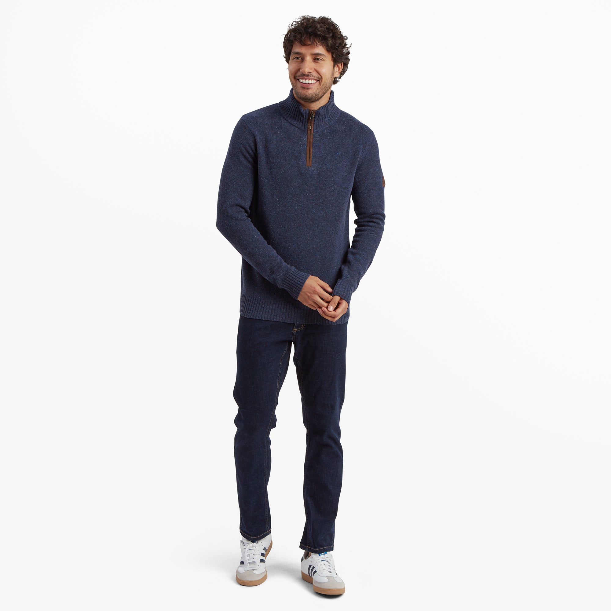 The man showcases a casual and modern outfit, combining the Sherpa Adventure Gear Kangtega Quarter Zip Sweater in Blue with dark jeans and white trainers, emphasising its versatile design suitable for various occasions.