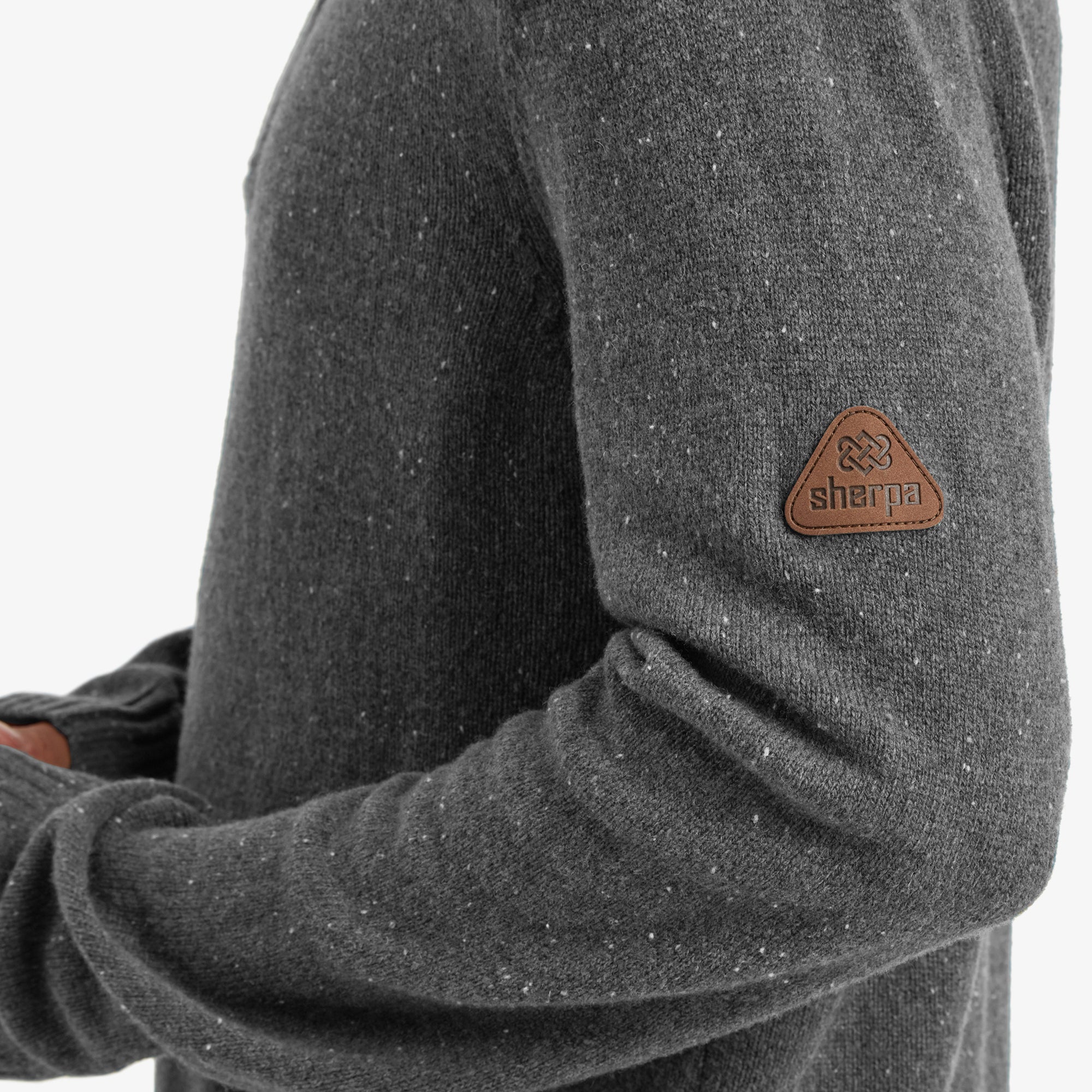 A close-up of the left sleeve, featuring a triangular Sherpa logo patch in tan leather. The fabric texture and speckled details of the Sherpa Adventure Gear Kangtega Quarter Zip Sweater in Grey are highlighted in this detailed shot.