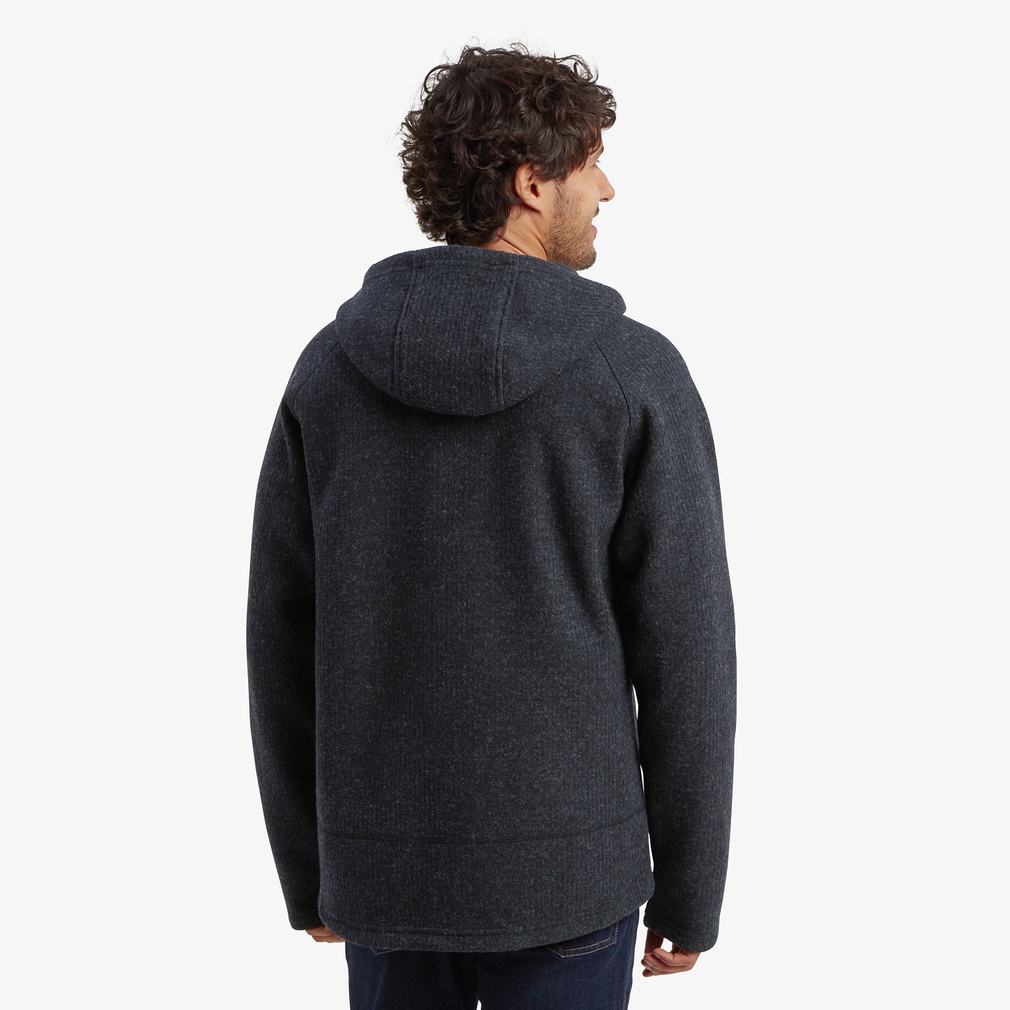 A back view of the Sherpa Adventure Gear Namgyal Hoodie in Black, showcasing the hood and a clean, seamless design across the shoulders and back. The heathered fabric texture is visible, paired with dark jeans for a cohesive look.