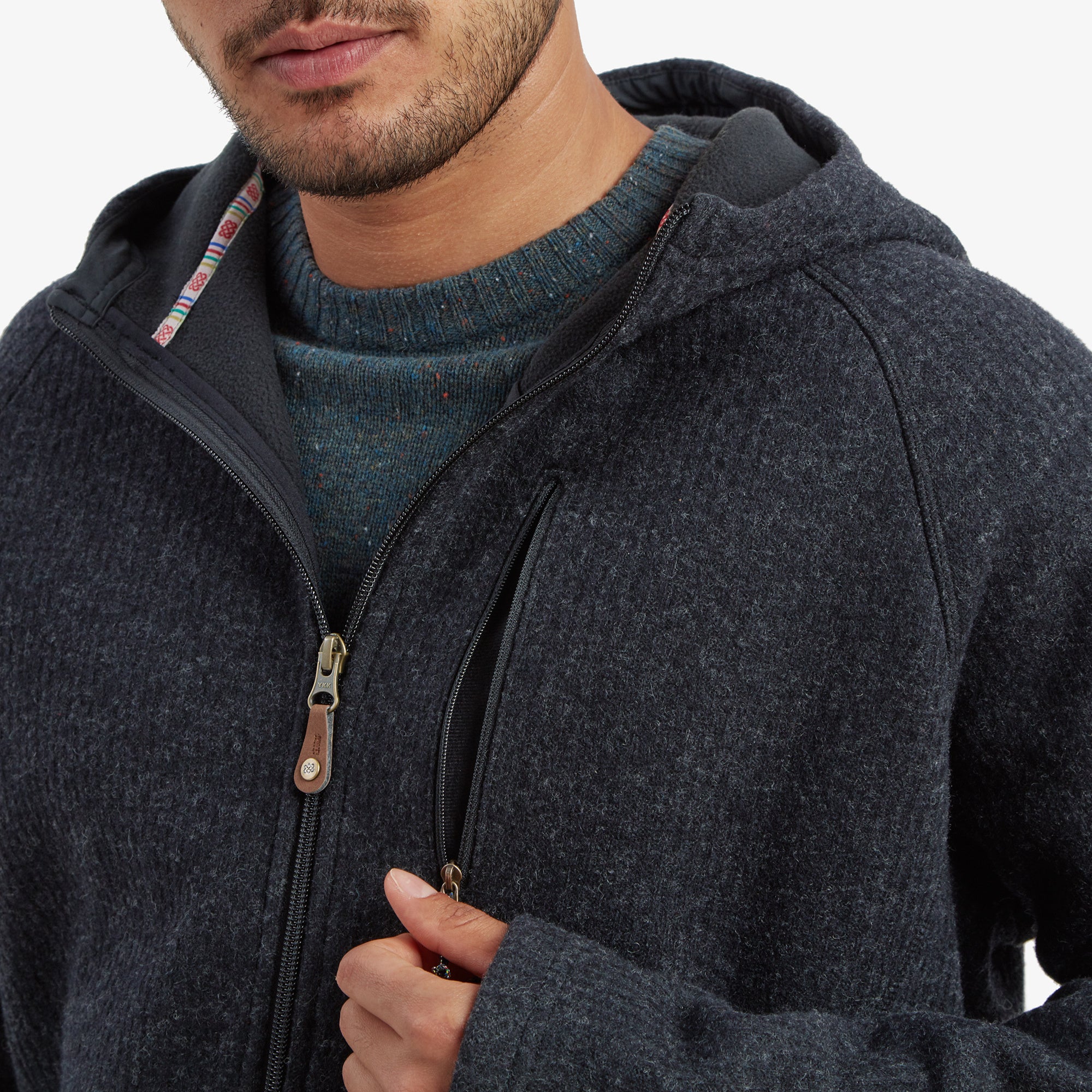 A closer view of the chest area of the Sherpa Adventure Gear Namgyal Hoodie in Black, showcasing the diagonal zippered chest pocket and the cozy fleece-like interior peeking out from under the jacket. The zip pull details include a leather accent.