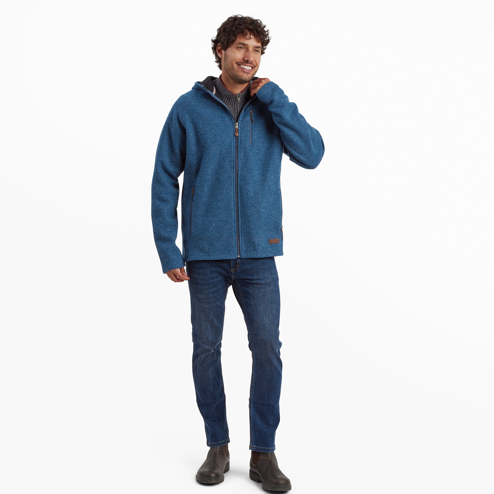 A full-body view of the same model in the Sherpa Adventure Gear Namgyal Hoodie in Blue. He pairs the hoodie with dark blue jeans and boots, exuding a casual, outdoorsy vibe. The hoodie’s fitted style and comfortable fabric are prominently showcased.