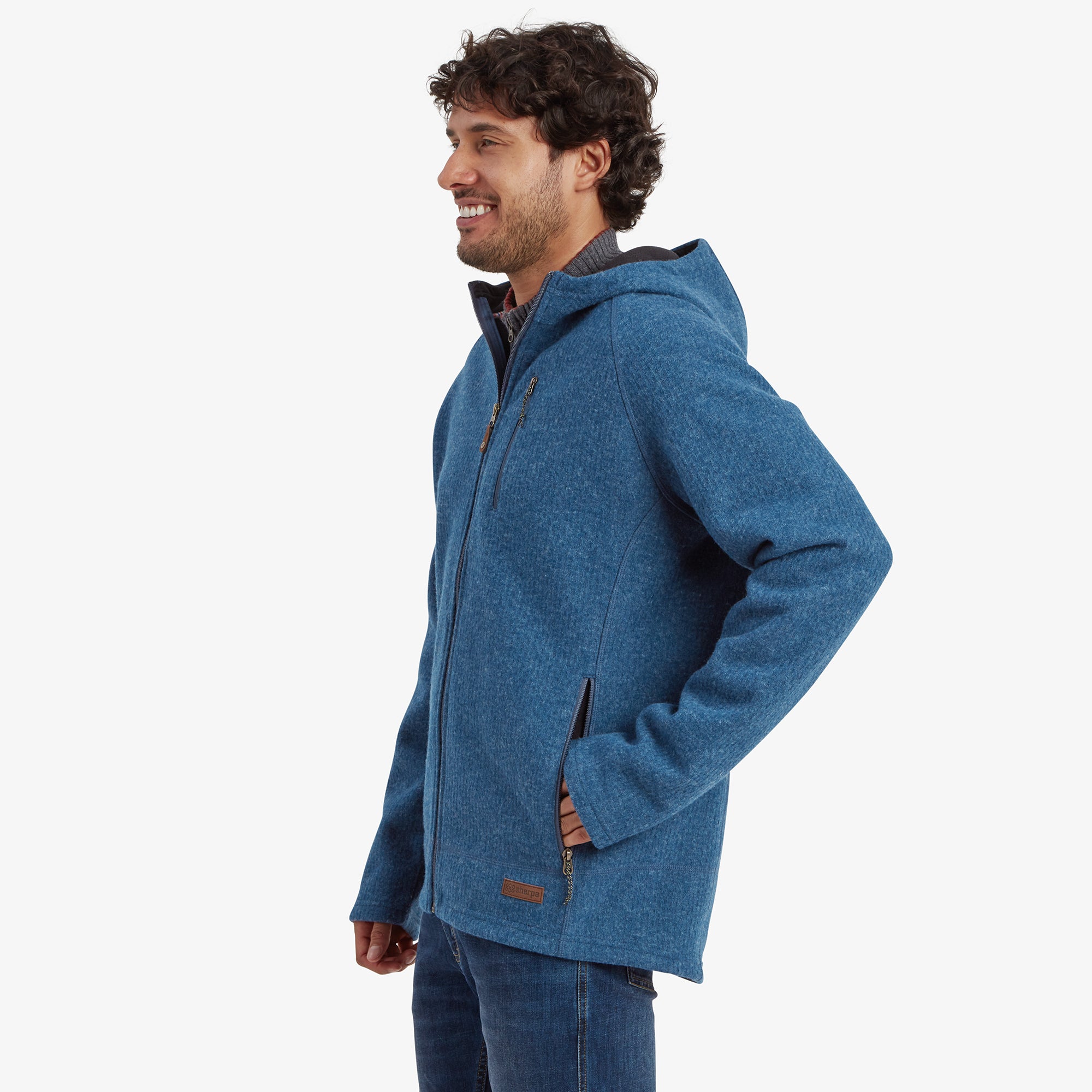 A side view of the model wearing the Sherpa Adventure Gear Namgyal Hoodie in Blue. This angle highlights the hoodie’s streamlined fit, the functional chest pocket with a zipper, and the layered collar detail peeking through from underneath.