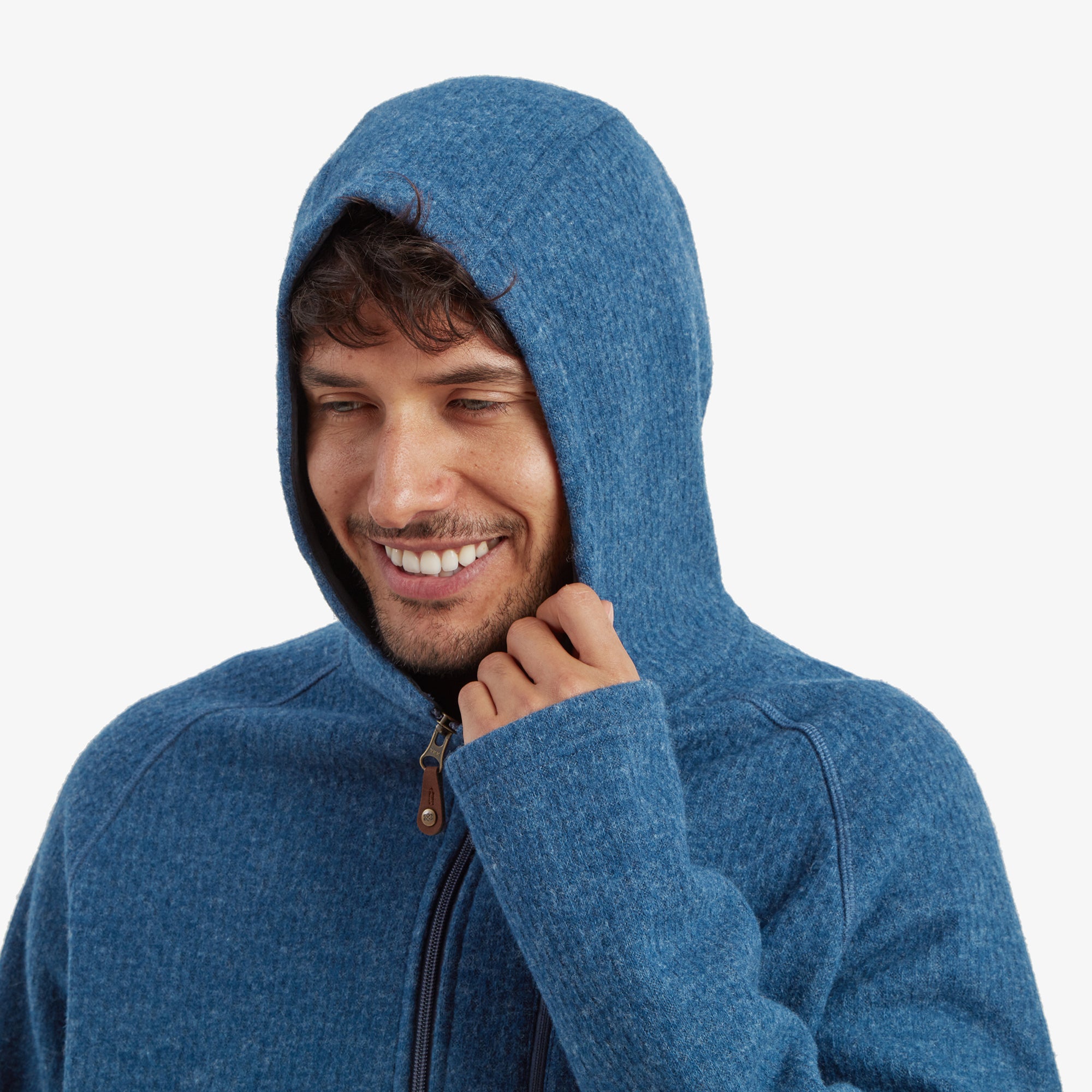 The model pulling the hood of the Sherpa Adventure Gear Namgyal Hoodie in Blue over his head, smiling warmly. The hood fits snugly, and the cozy interior of the hoodie is visible.