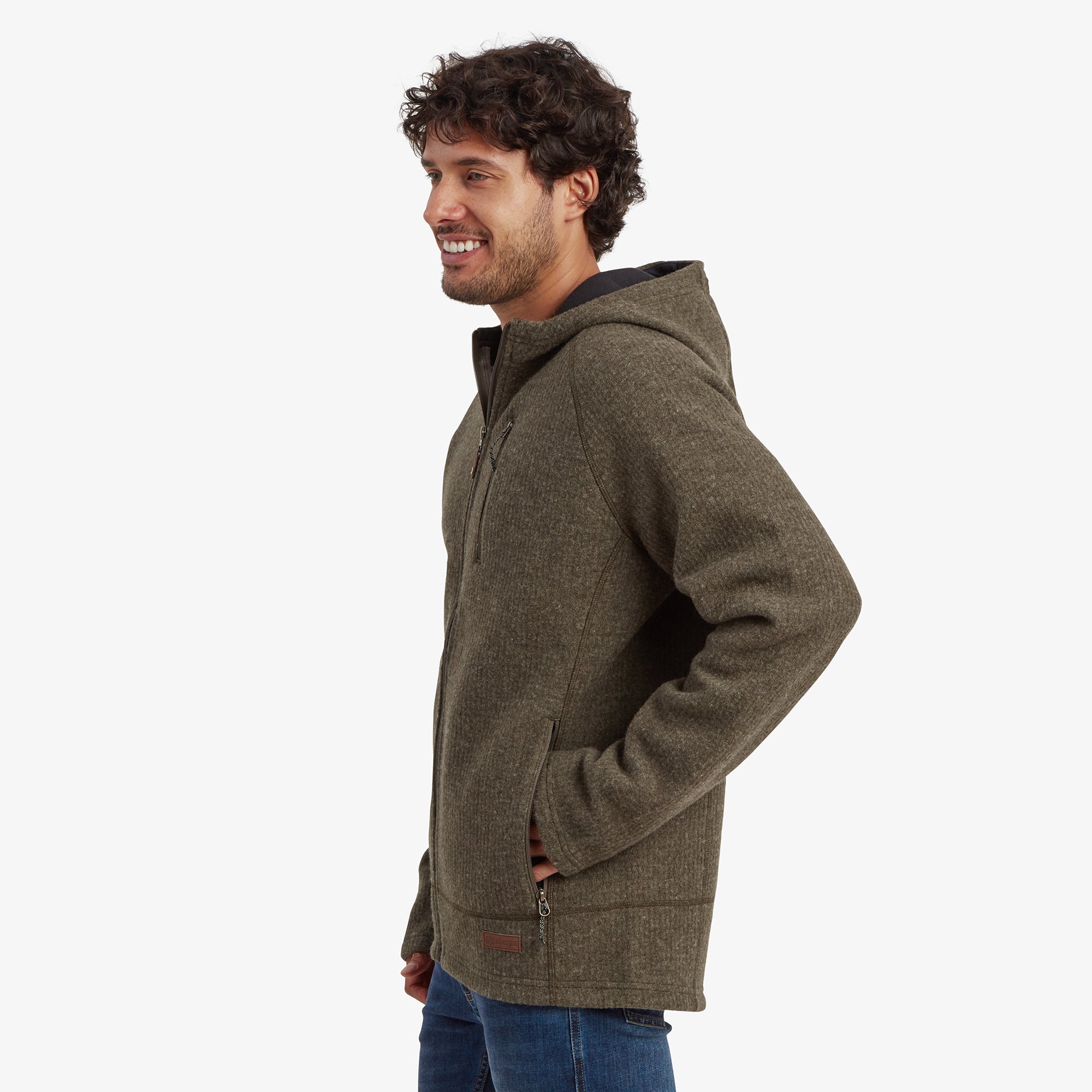 A side profile of the model wearing the Sherpa Adventure Gear Namgyal Hoodie in Green. The image emphasises the hood's structure, raglan sleeves, and side zippered hand pockets, with the fabric texture being prominently visible.