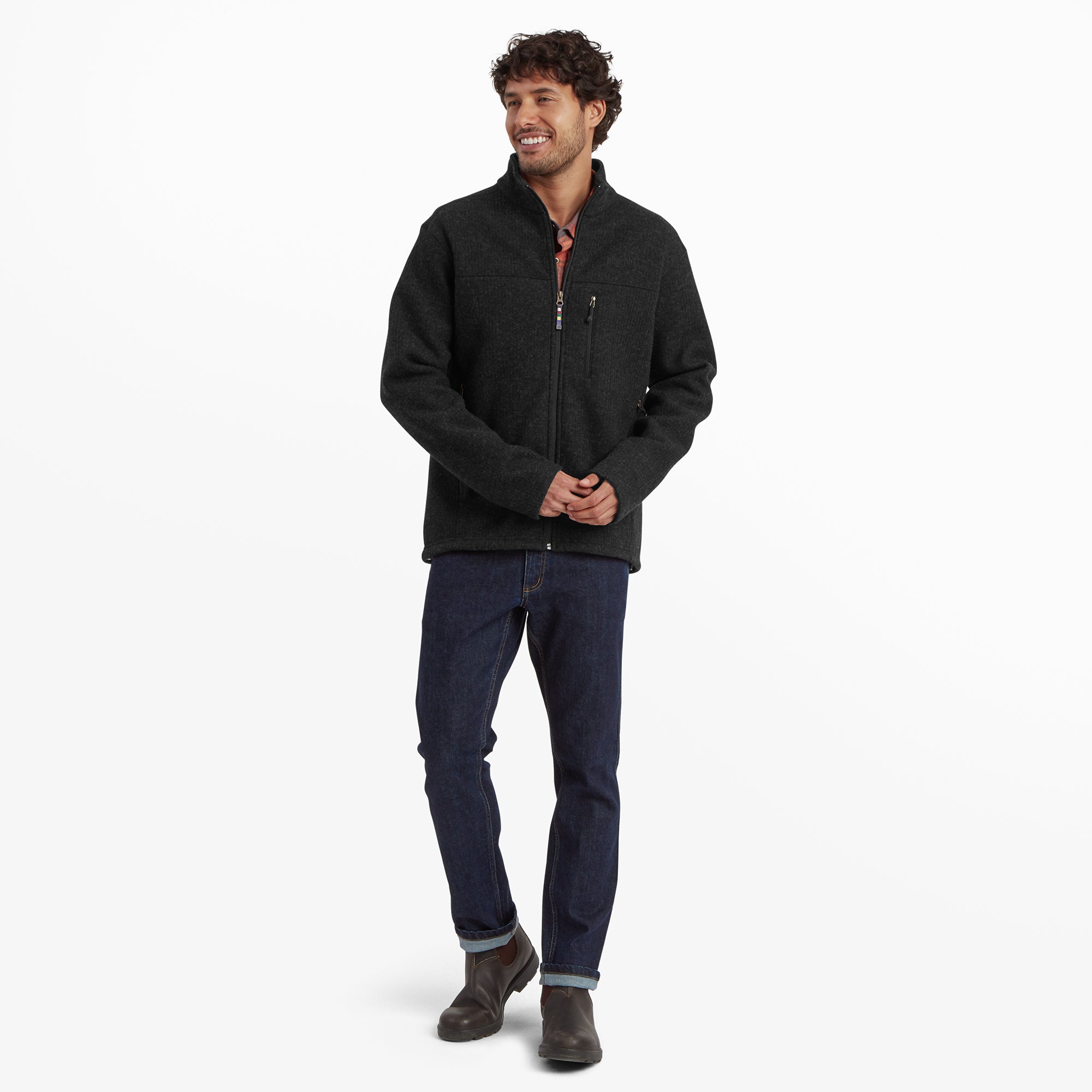 The same man is seen standing in a relaxed pose, wearing the Sherpa Adventure Gear Namgyal Jacket in Black fully zipped. He pairs the jacket with dark jeans and boots, exuding a casual and outdoor-ready style.