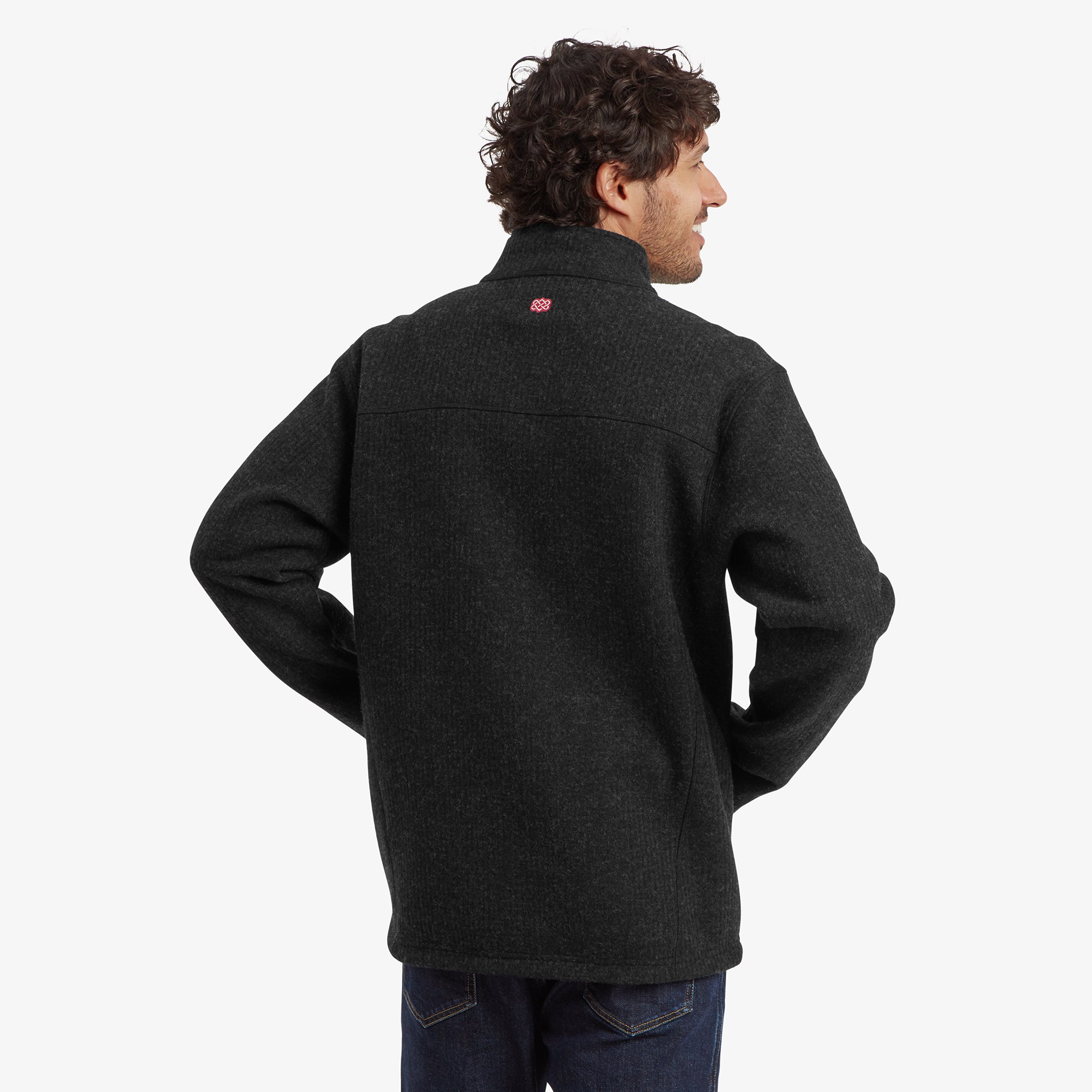 A back view of the Sherpa Adventure Gear Namgyal Jacket in Black, showcasing its seamless design and subtle Sherpa logo detail below the collar.