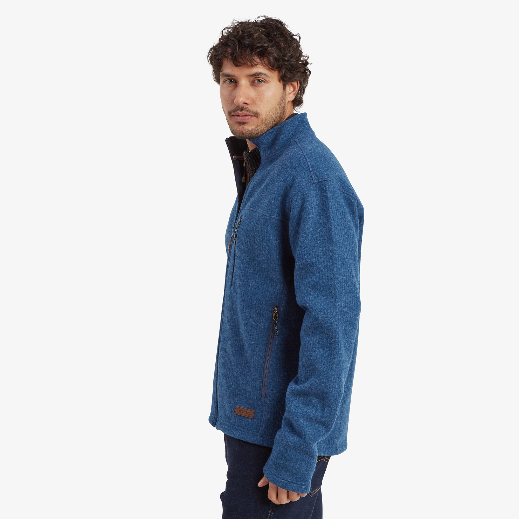 Side view of the model wearing the Sherpa Adventure Gear Namgyal Jacket in Blue. The jacket’s side seam, shoulder stitching, and profile of the chest pocket zipper are visible. The model’s hands are in his pockets, and the background is plain off-white.