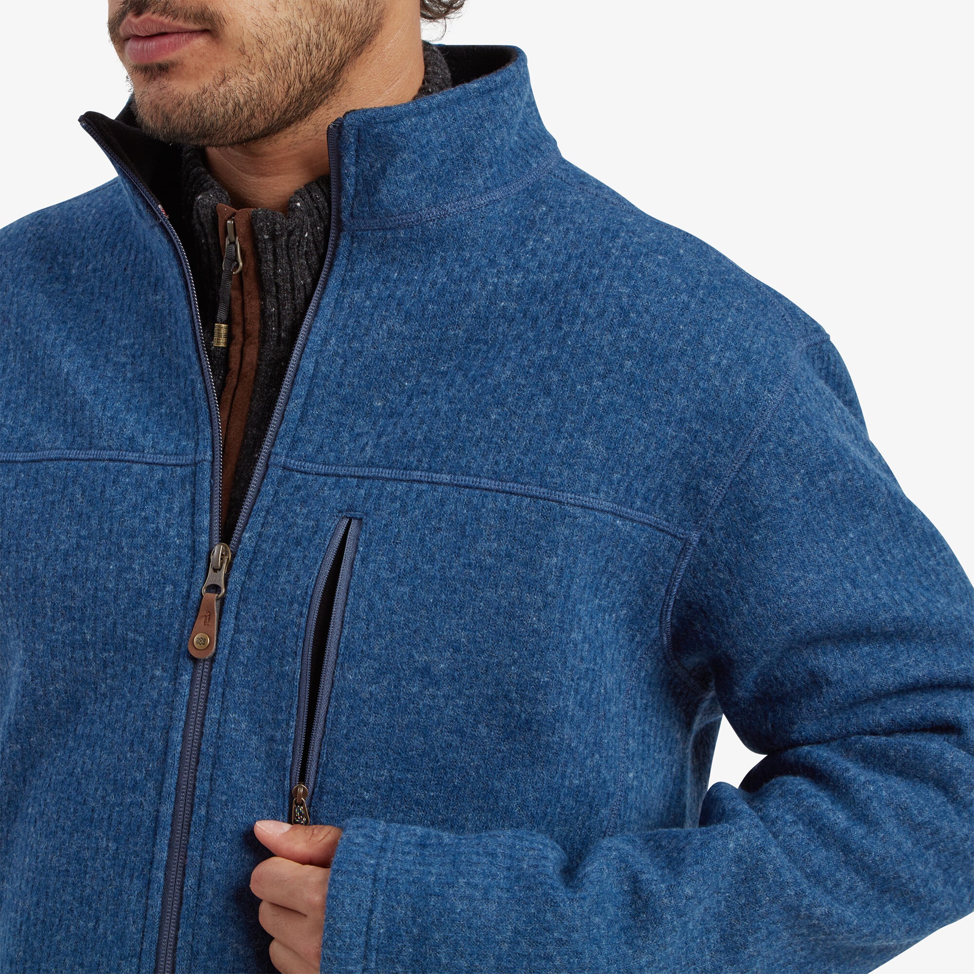 Detailed view of the chest pocket zipper and the main front zipper on the Sherpa Adventure Gear Namgyal Jacket in Blue. Both zippers have leather pull tabs with decorative braided cords attached. The textured knit fabric and neat stitching are clearly visible, showing the high-quality construction. The background is plain off-white.