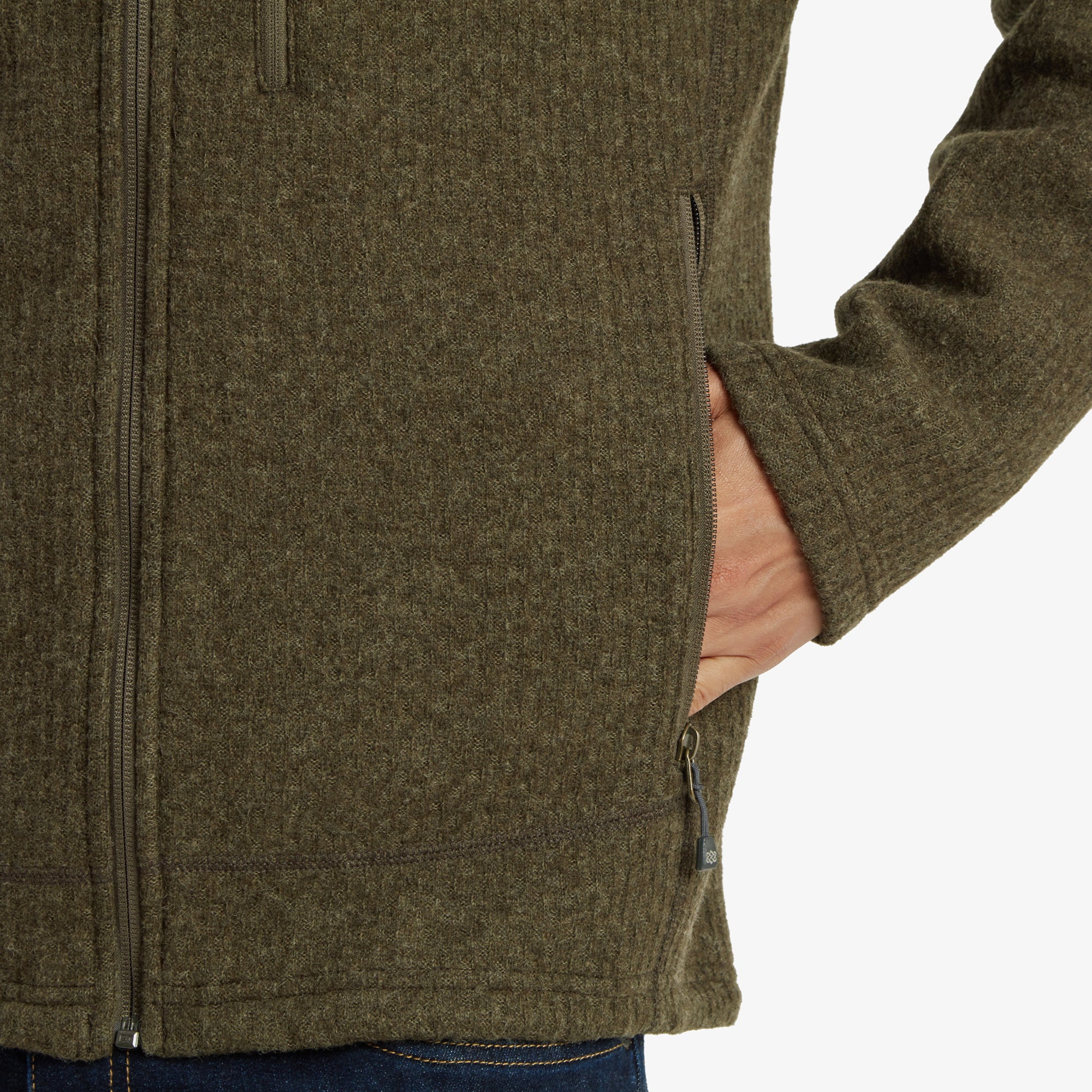 A detailed view of the front chest area of the Sherpa Adventure Gear Namgyal Jacket in Brown, showcasing the Sherpa Adventure Gear logo embroidered on the fabric. The zippered chest pocket with a colorful pull-tab adds a touch of functionality and style, enhancing the jacket’s overall design.