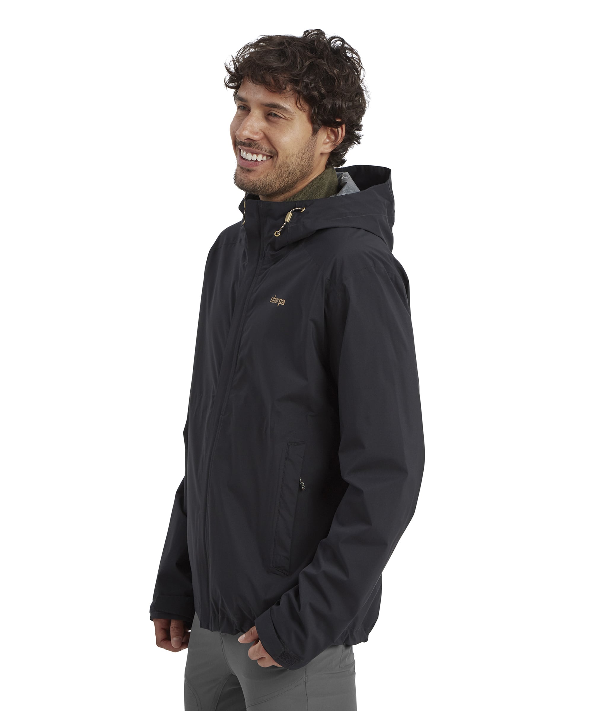 A side profile of the model in the same Sherpa Adventure Gear Nima 2.5-Layer Jacket in Black, highlighting the jacket's fitted design and hood. The model is smiling and glancing sideways.