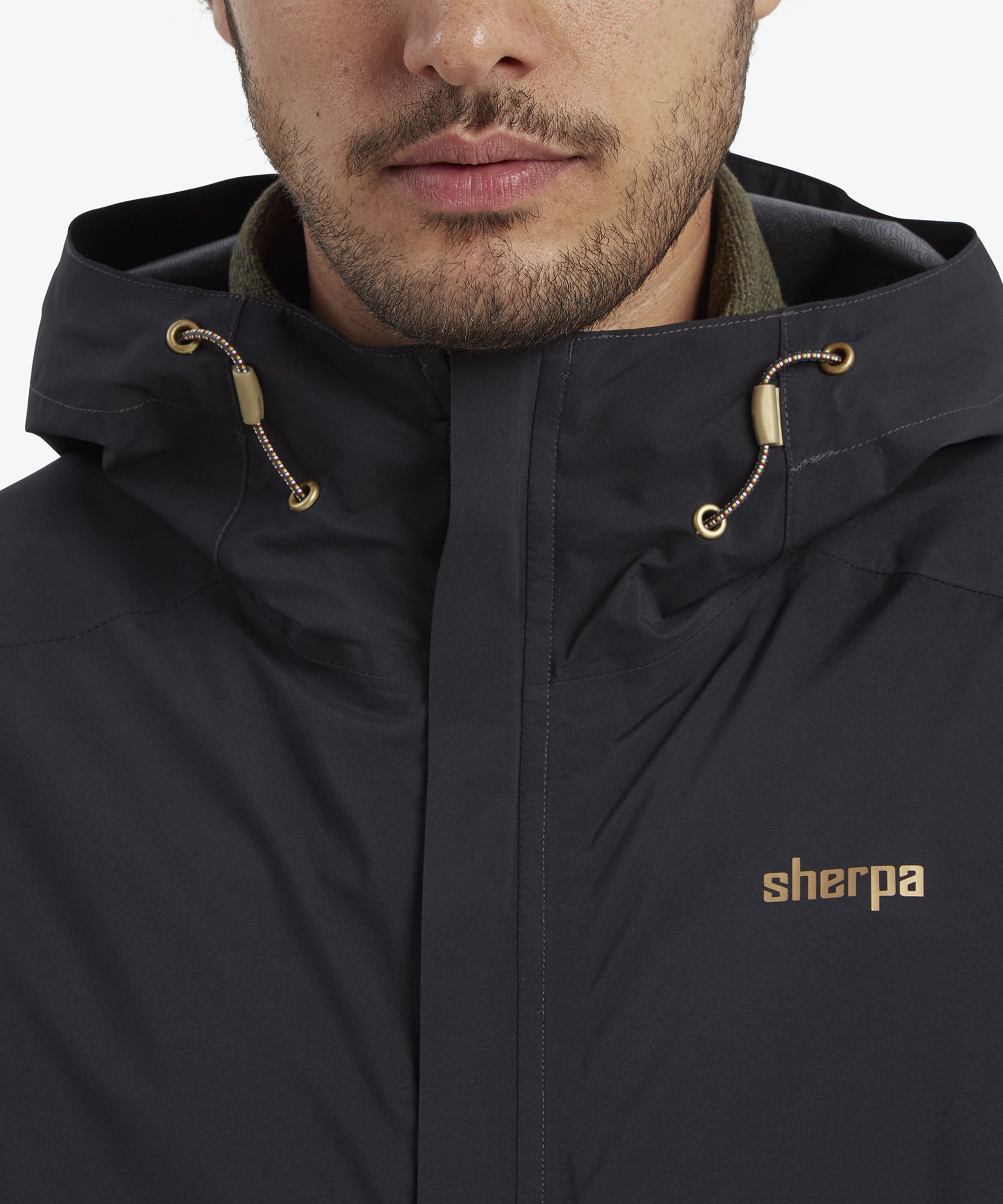 A close-up image focusing on the hood and upper part of the Sherpa Adventure Gear Nima 2.5-Layer Jacket in Black. The model wears the hood, showcasing its adjustable drawstrings and snug fit for outdoor protection.