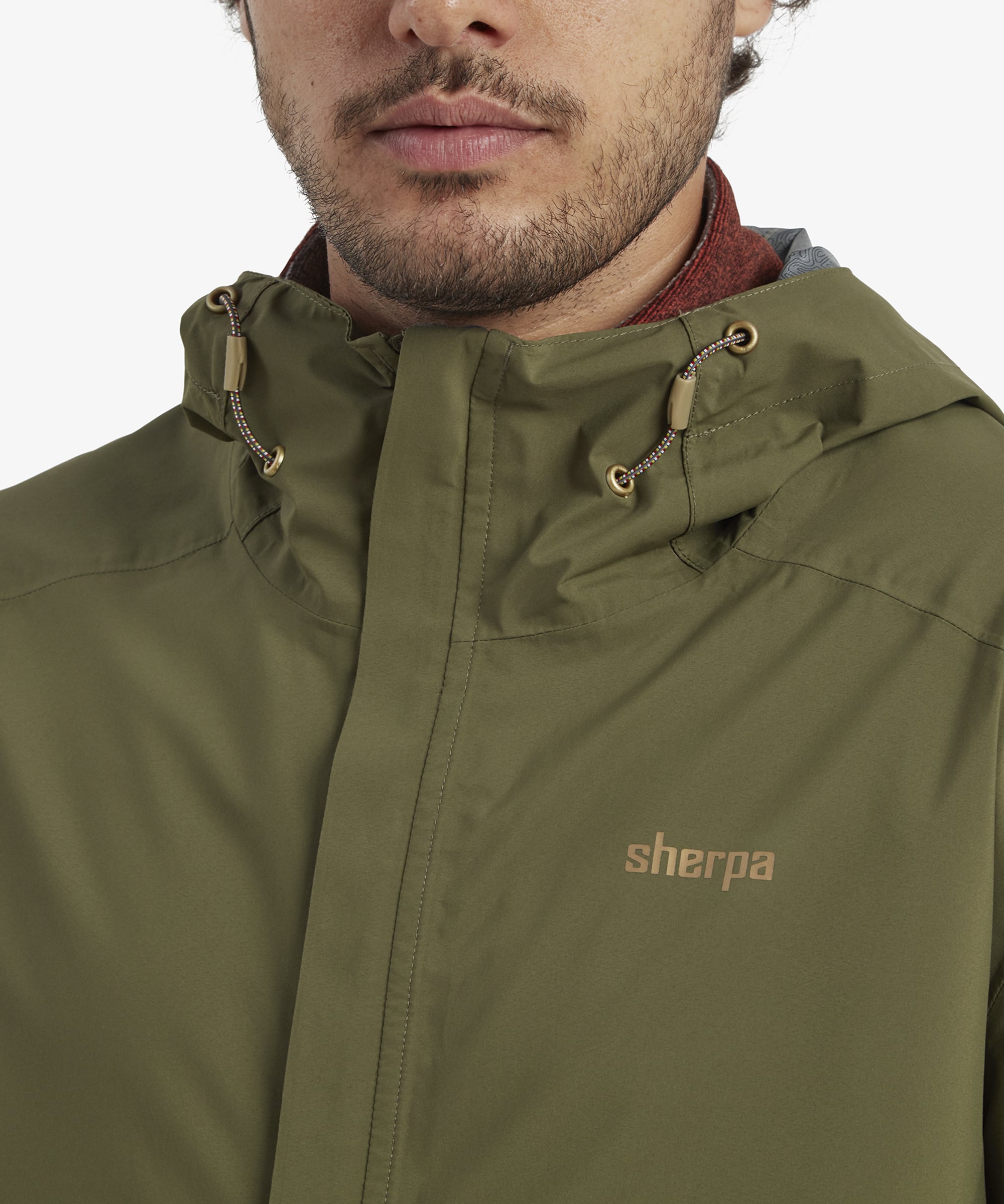 A close-up view of the man wearing the Sherpa Adventure Gear Nima 2.5-Layer Jacket in Green with the hood on. The drawstring adjustments on the hood are visible, demonstrating its functionality for protecting against the elements. The man’s expression conveys comfort and ease.