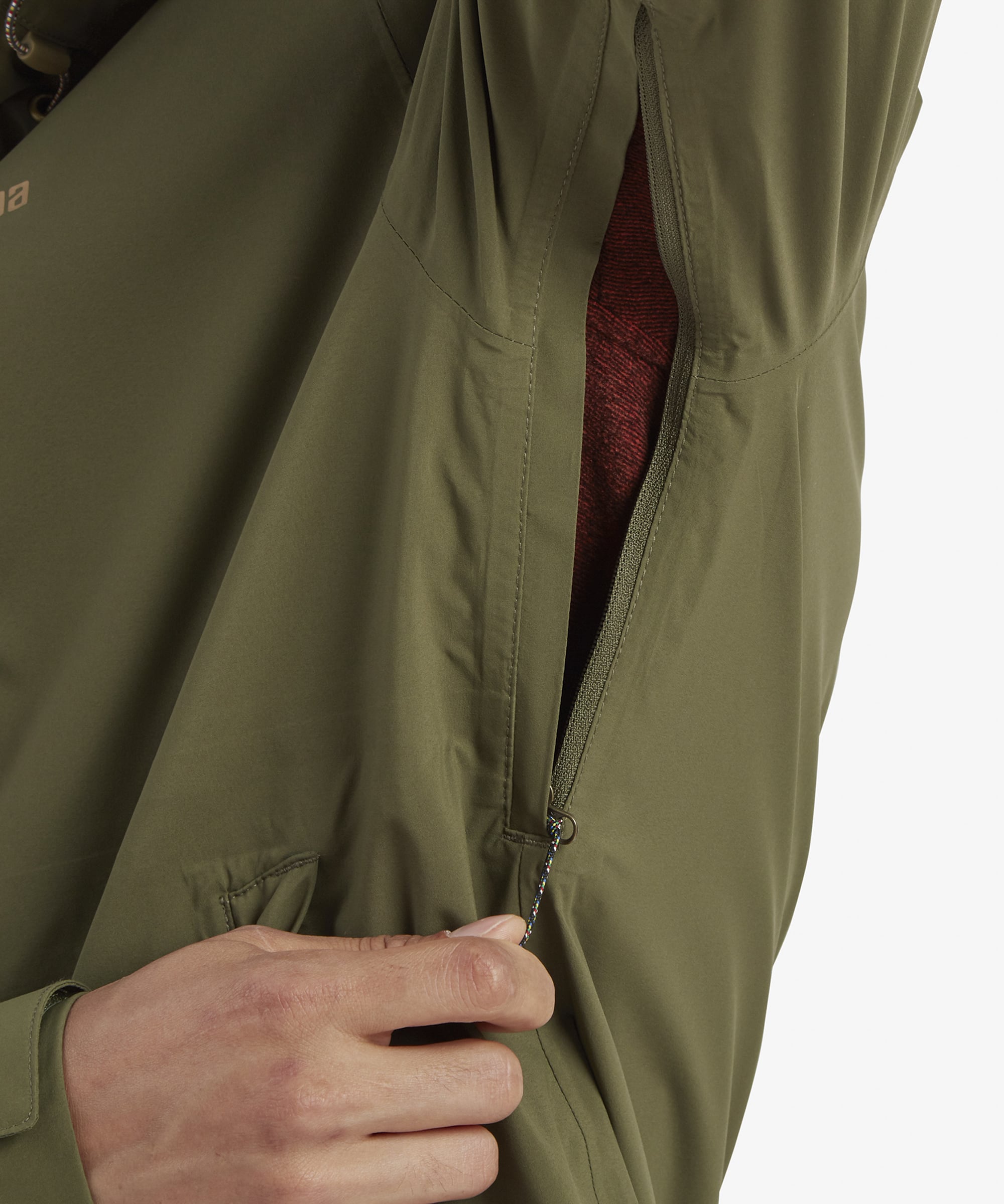 A close-up of the underarm area, featuring a zippered ventilation opening. The bright red interior lining is visible, showcasing the breathable design of the Sherpa Adventure Gear Nima 2.5-Layer Jacket in Green for active use.