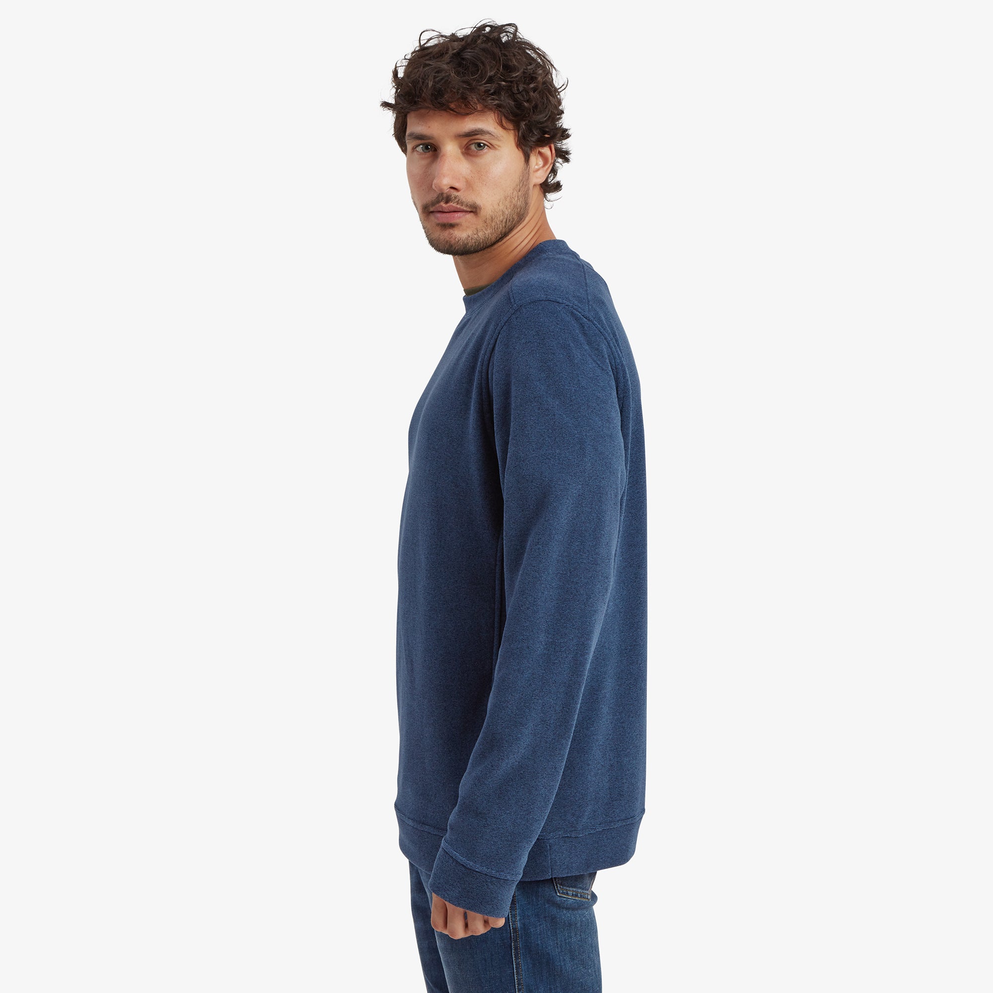 A side profile view of the man wearing the Sherpa Adventure Gear Rolpa Eco Crew in Blue. The shot highlights the simple and clean side details of the sweatshirt, emphasising its tailored fit and soft fabric.