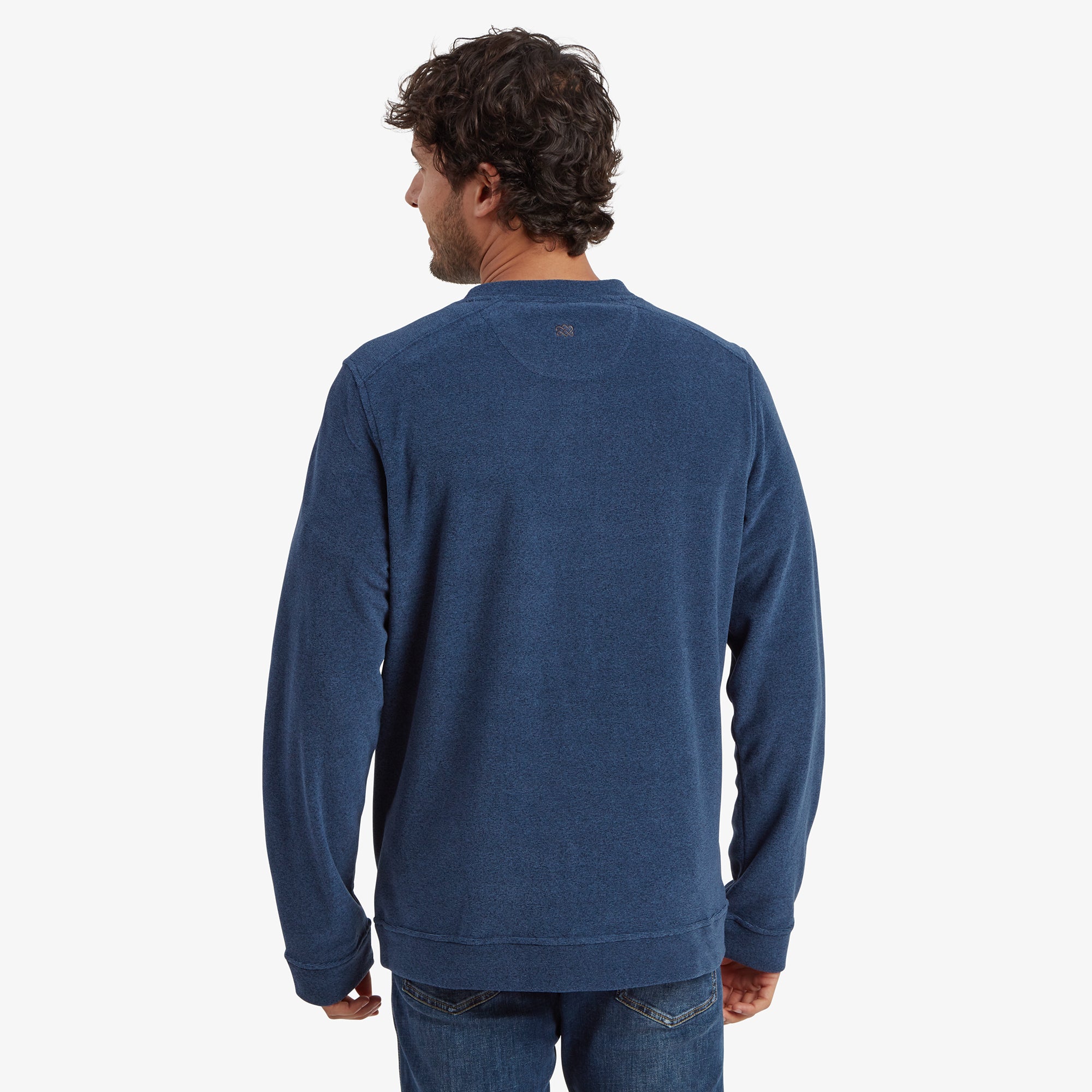 The back view of the model wearing the Sherpa Adventure Gear Rolpa Eco Crew in Blue, showing its clean lines and subtle details, including a small tonal logo near the neckline. The sweatshirt’s length provides coverage over the waistband of the jeans, contributing to its comfortable fit.