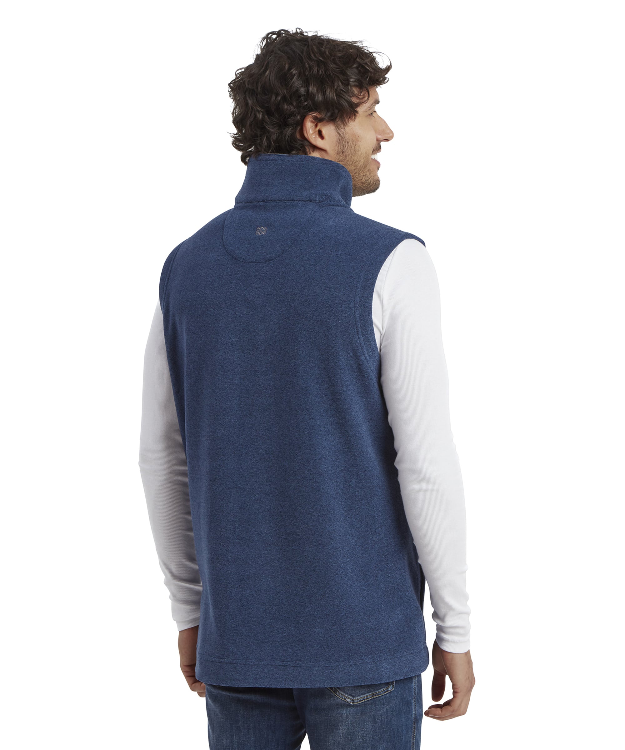 Rear view of the Sherpa Adventure Gear Rolpa Eco Vest in Blue, showing the clean back design. The vest features a slightly raised collar, and a small embroidered logo near the upper back. The man is turned slightly to his left, providing a clear view of the vest’s back and side seams.