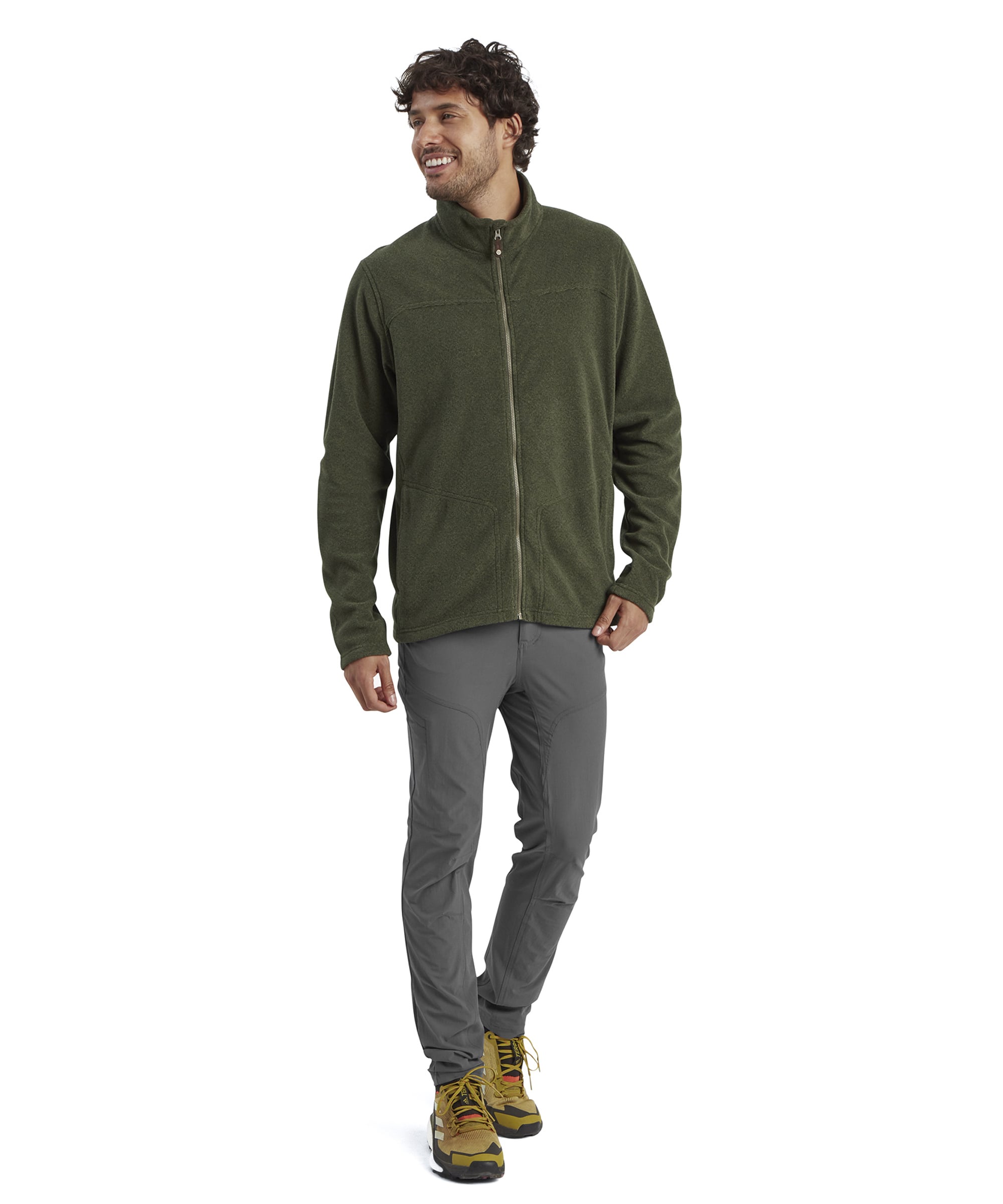 The same man is captured in a full-body shot, showcasing the Sherpa Adventure Gear Rolpa Eco Jacket in Green paired with gray trousers and yellow hiking shoes. He is smiling and walking forward, giving a relaxed and outdoor-friendly vibe.