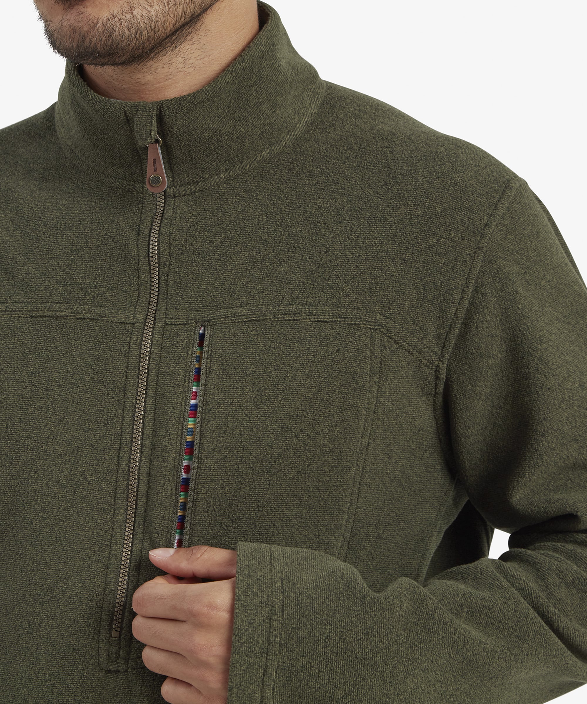 A close-up of the chest area of the Sherpa Adventure Gear Rolpa Eco Quarter Zip in Green, showcasing the detailed chest pocket zipper with a multicolored trim and the branded zipper pull. The close-up emphasises the garment's attention to detail and craftsmanship, ideal for versatile outdoor or casual use.