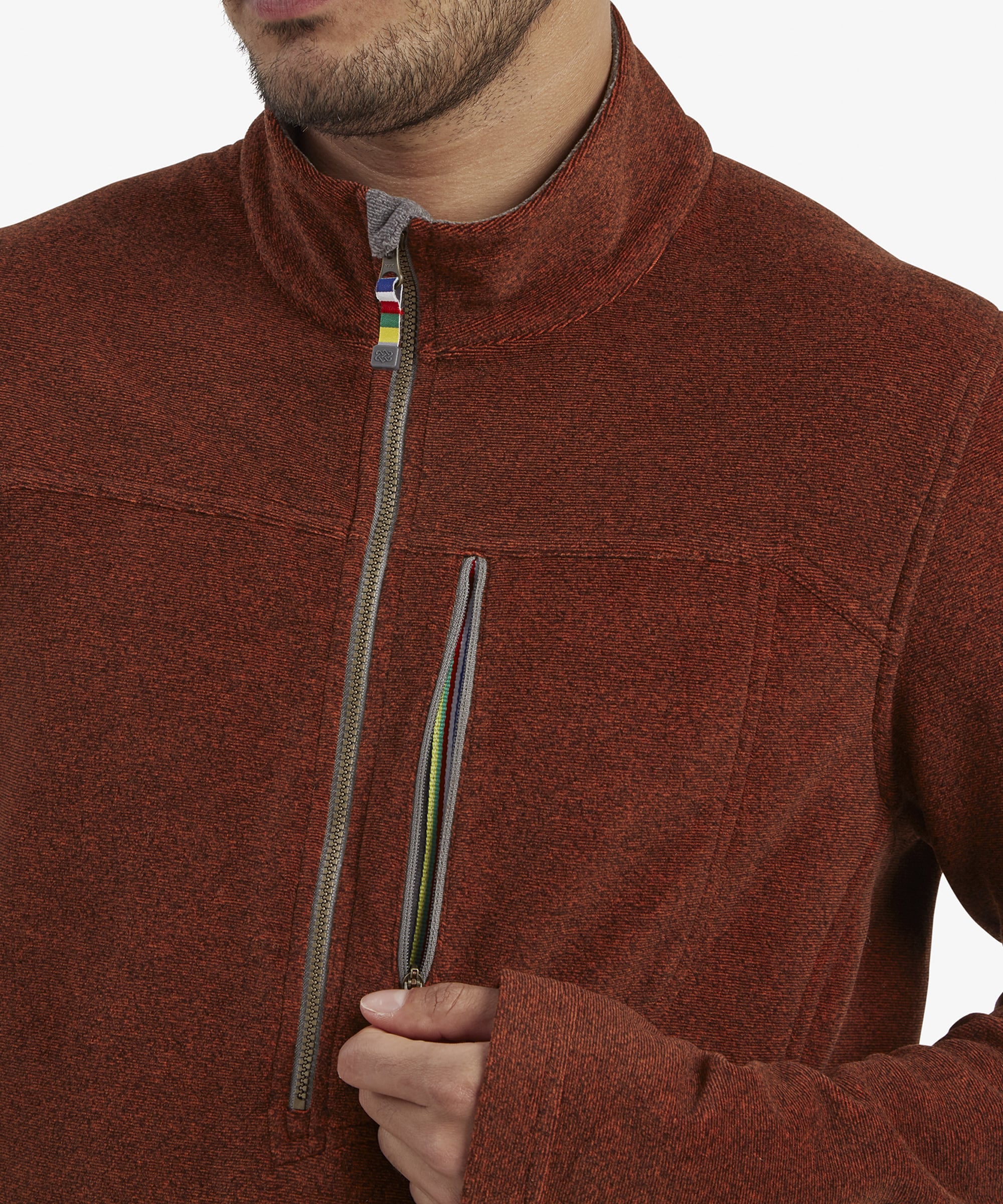 A close-up of the chest area of the Sherpa Adventure Gear Rolpa Eco Quarter Zip in Red, focusing on the zippered pocket. The multicolored zipper pull is visible, adding a pop of vibrant detail to the otherwise monochromatic fleece. The texture of the material and the sturdy stitching are prominently displayed.