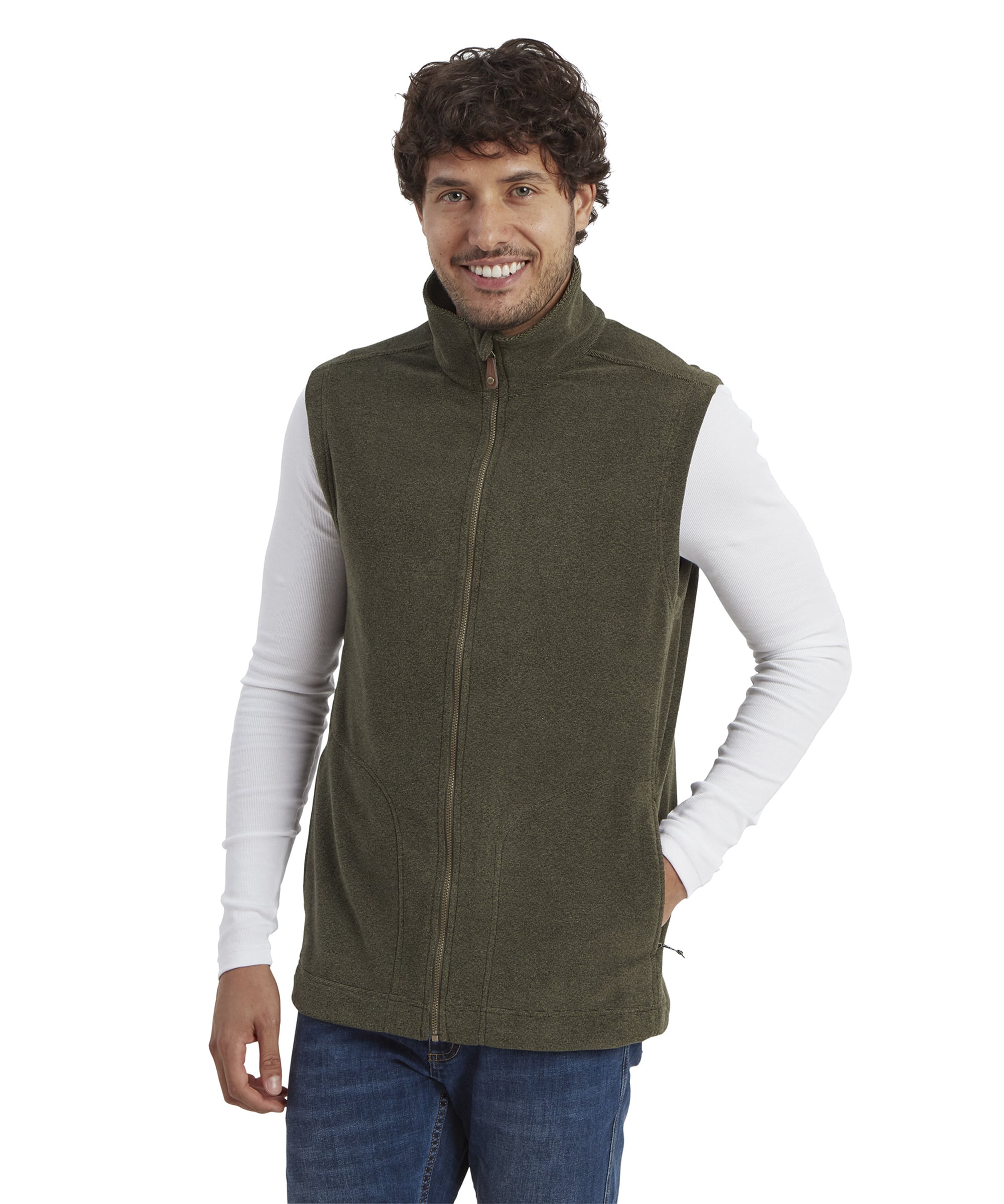 A smiling man wearing a Sherpa Adventure Gear Rolpa Eco Vest in Green, paired with a white long-sleeve shirt and blue jeans. The vest features a high collar and a front zipper. He has one hand casually resting in his pocket, conveying a relaxed look.