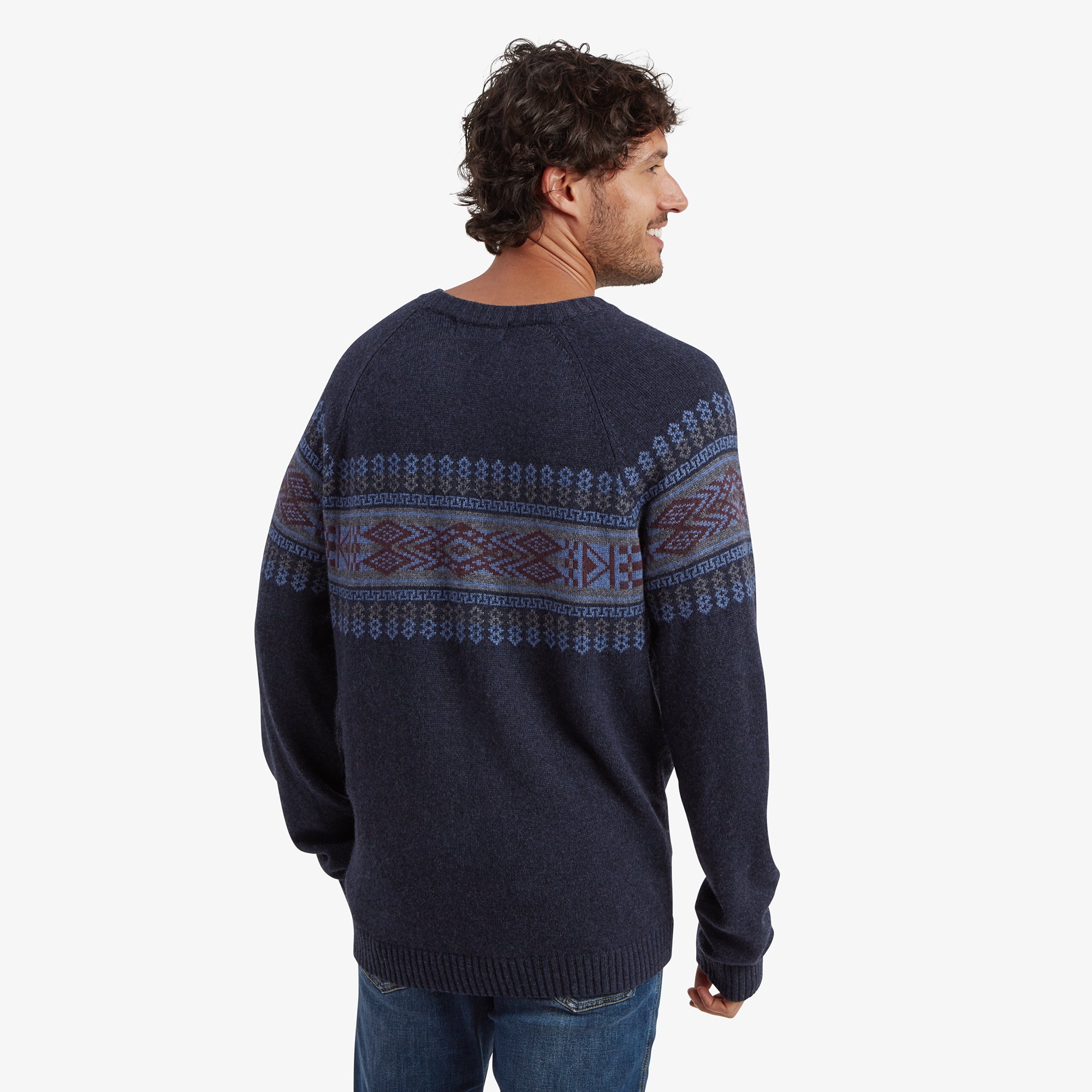 The man is facing away from the camera, revealing the back of the Sherpa Adventure Gear Sajit Eco Crew in Blue. The geometric pattern wraps around the upper back, while the lower section is plain navy blue.