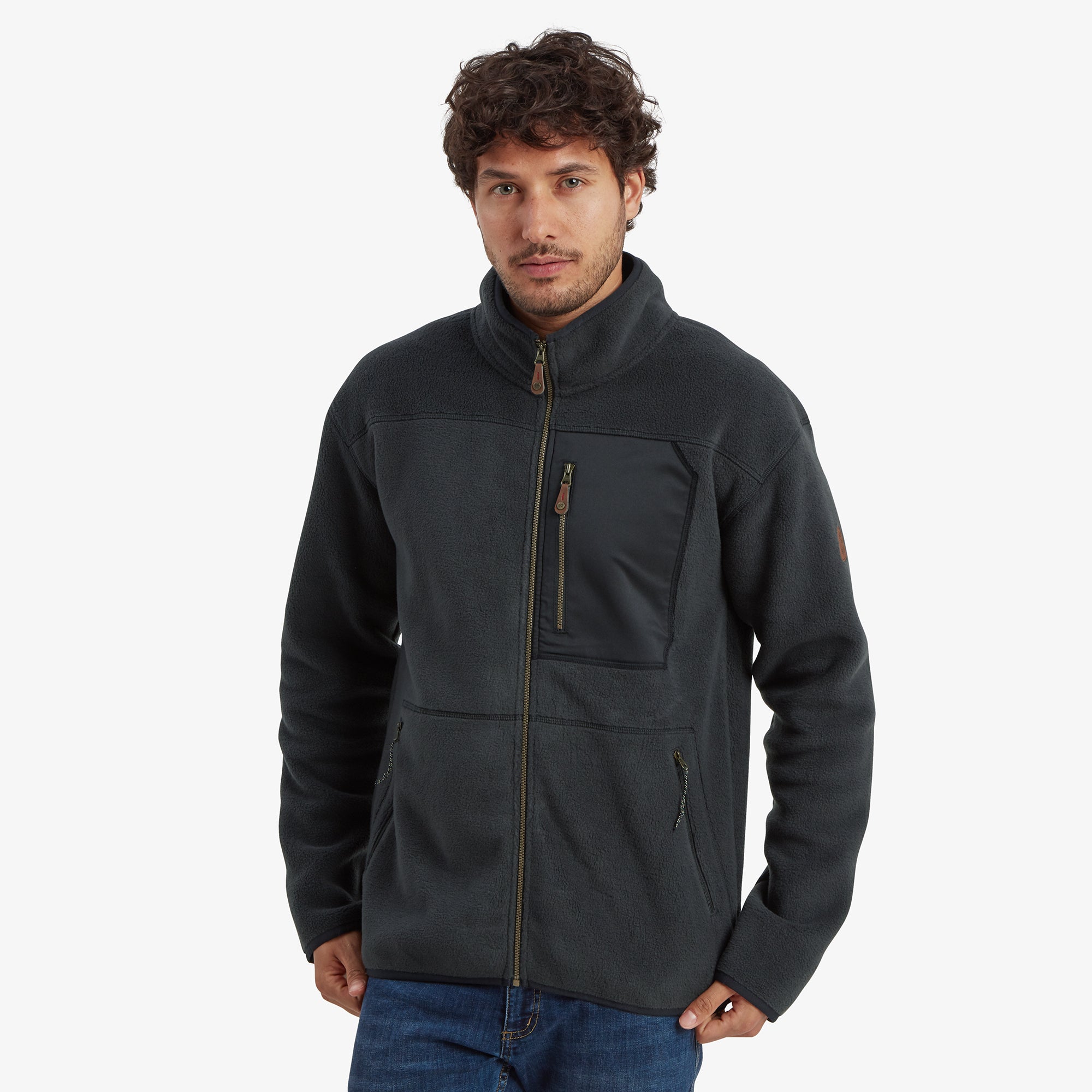 A man wearing a Sherpa Adventure Gear Sanani Eco Fleece Jacket in Black with a high collar and full front zipper, standing confidently while showcasing the jacket's functional chest pocket with a zipper. The jacket's design features a sleek and minimalistic look.