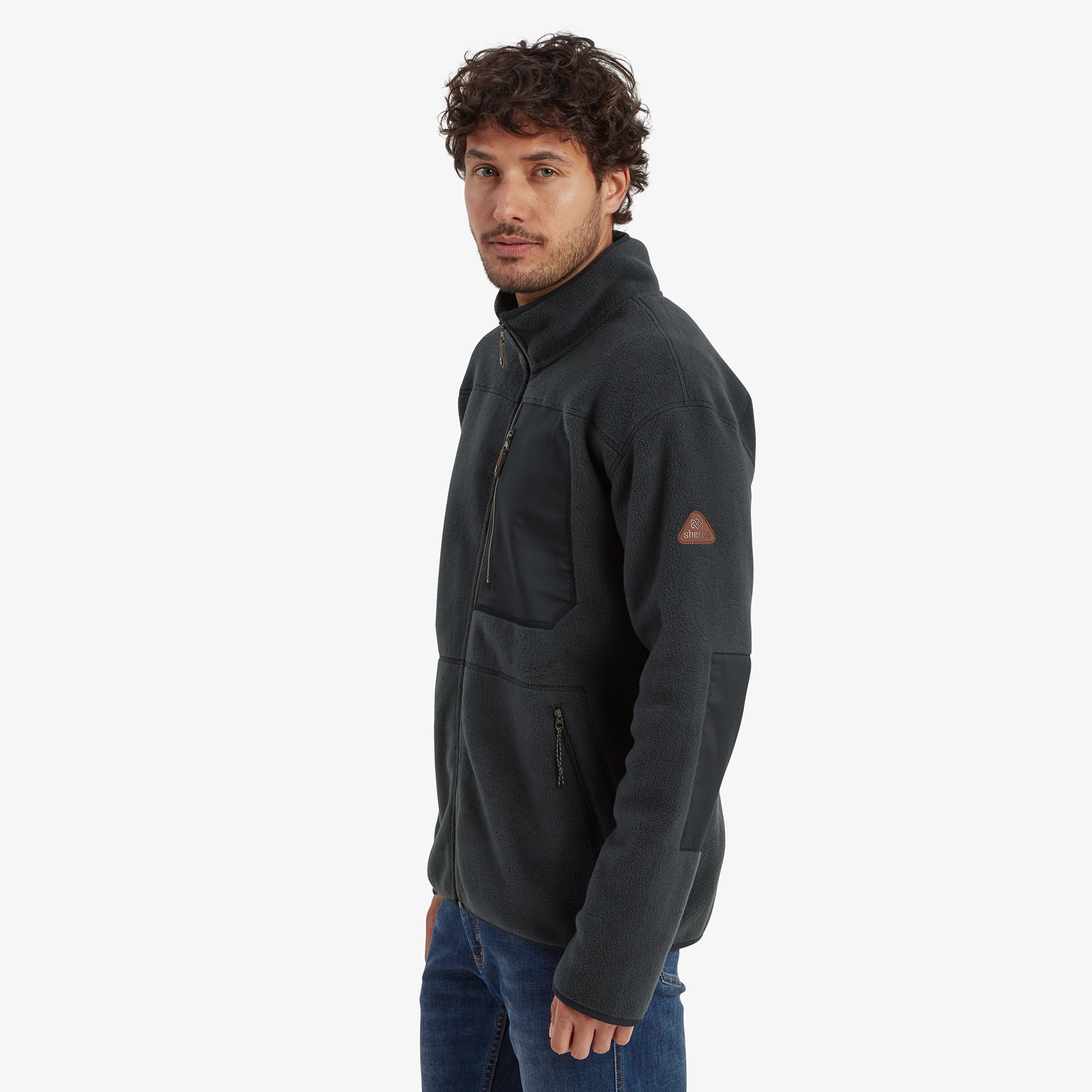 A smiling model turned slightly to the side, displaying the left sleeve with a small logo patch and the Sherpa Adventure Gear Sanani Eco Fleece Jacket in Black’s side panel. The image captures the jacket's ergonomic fit and aesthetic details.