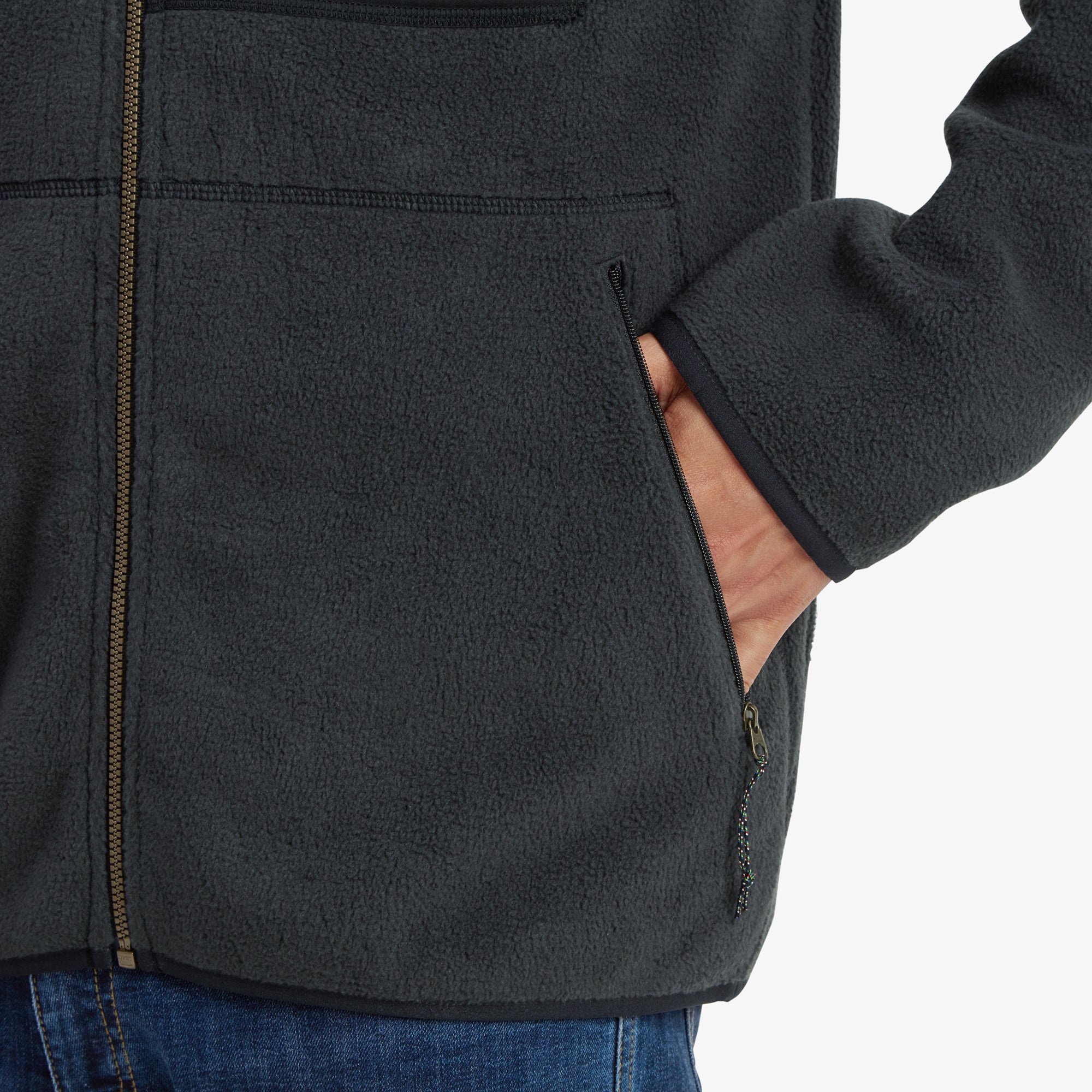 A close-up of the side pocket with a model's hand partially tucked inside, highlighting the Sherpa Adventure Gear Sanani Eco Fleece Jacket in Black's warm and practical side pockets with zippers for secure storage.