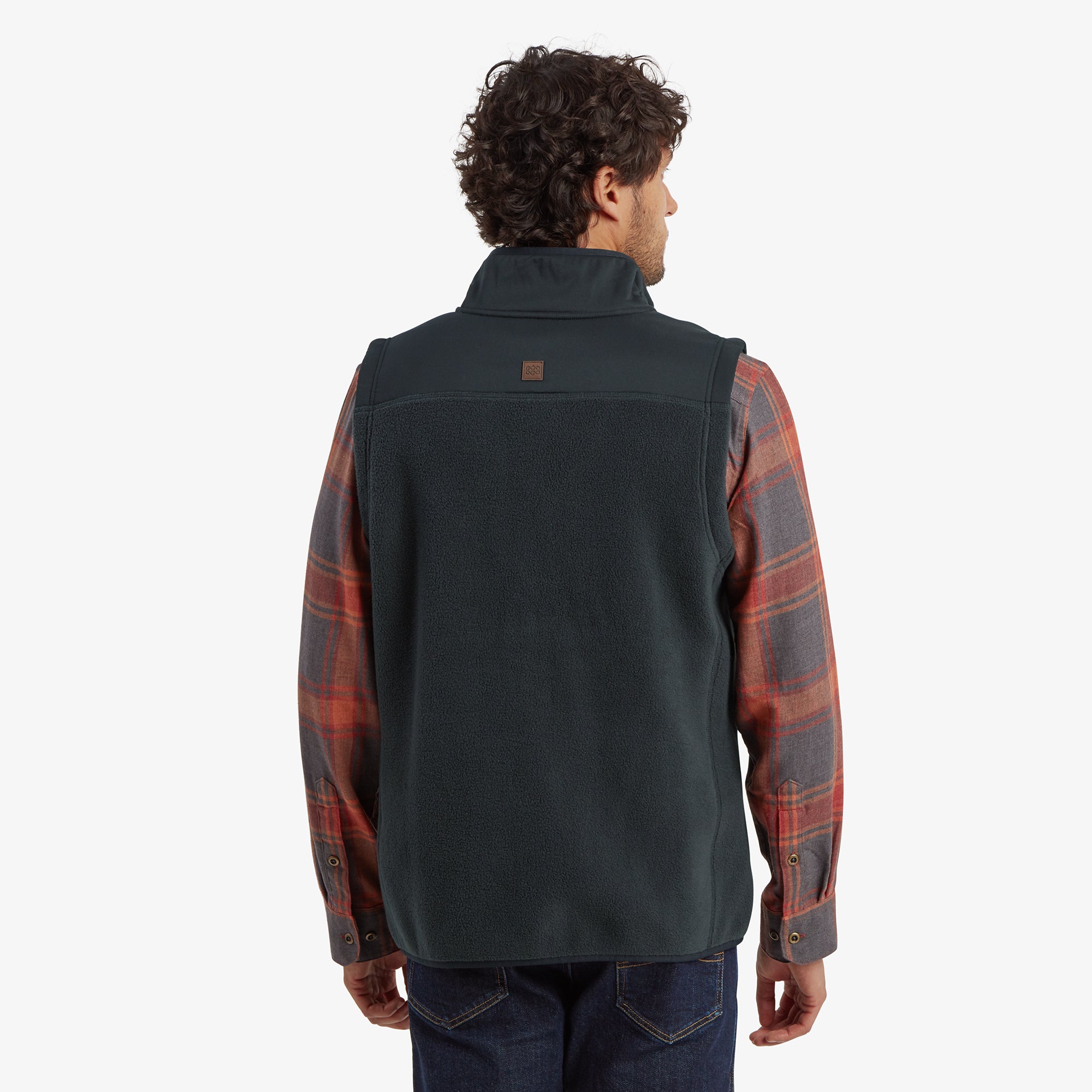 A rear view showing the Sherpa Adventure Gear Sanani Eco Fleece Vest in Black from the back. The vest has a slightly tailored design and a small logo patch on the upper back. The plaid shirt underneath is visible at the shoulders and cuffs.