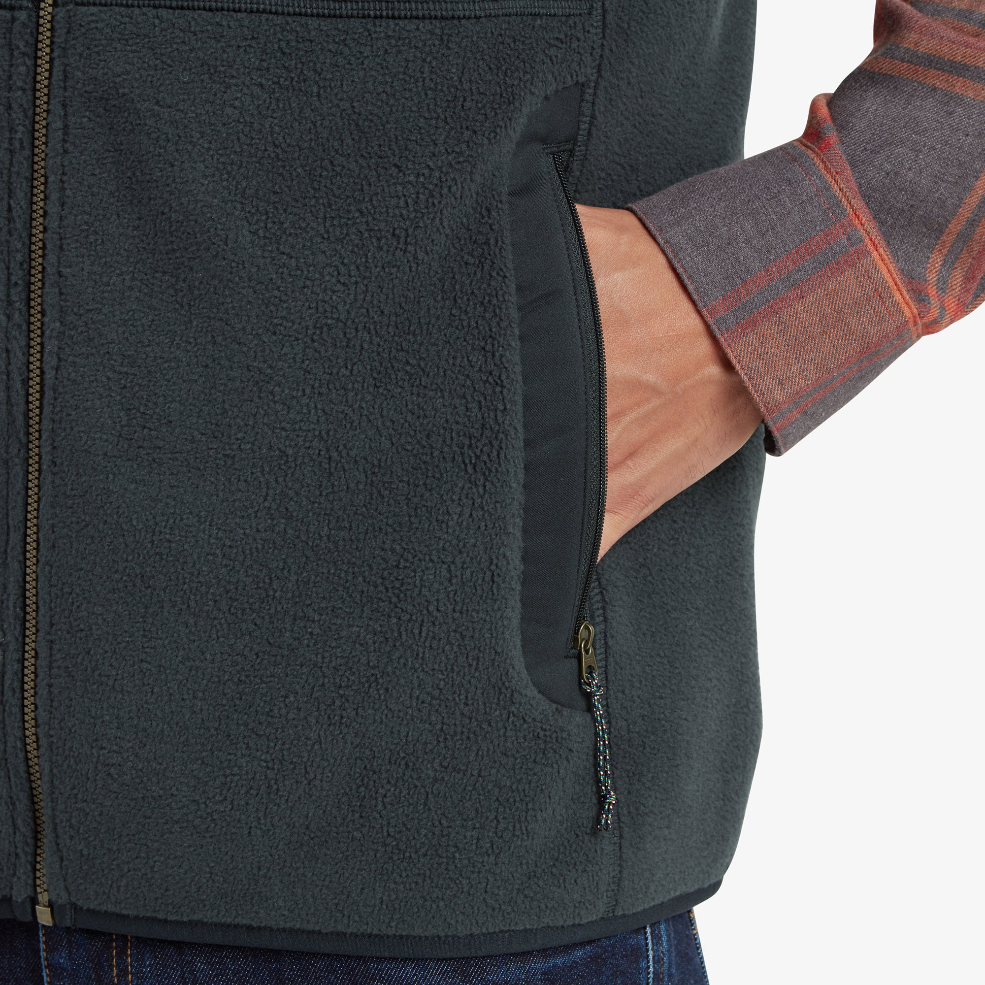 A close-up of one of the zippered hand pockets on the Sherpa Adventure Gear Sanani Eco Fleece Vest in Black. The man’s hand is inside the pocket, emphasising the comfortable and functional design of the fleece material and zippered closure.