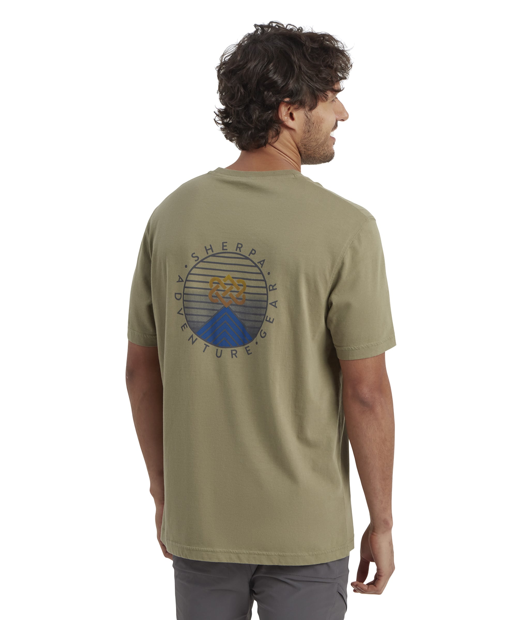 A side-profile view of the man wearing the Sherpa Adventure Gear Summit T-Shirt in Green. The model is smiling, and the relaxed fit of the t-shirt is evident, along with the hem reaching mid-hip.