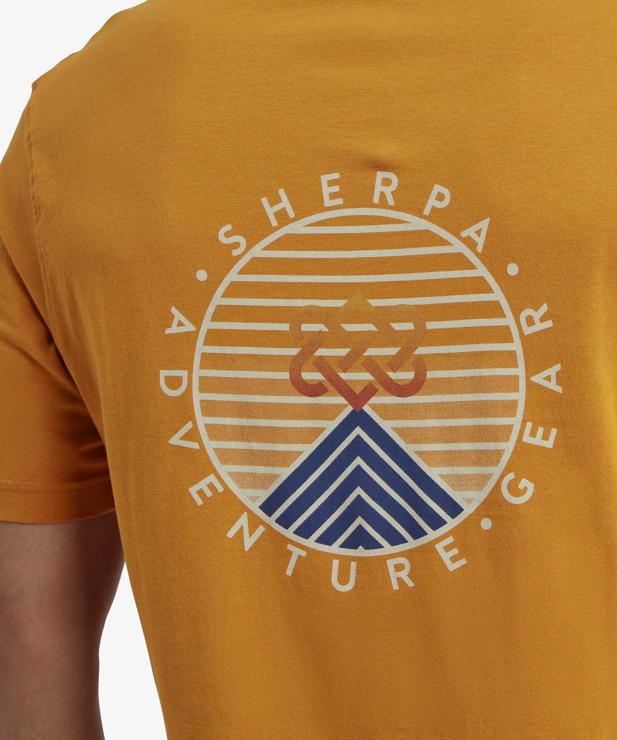 A focused view of the large back graphic on the Sherpa Adventure Gear Summit T-Shirt in Orange. The circular design has bold orange stripes and a blue geometric mountain shape at the bottom, with the Sherpa logo intertwined in the center. The words "Sherpa Adventure Gear" curve around the circle.