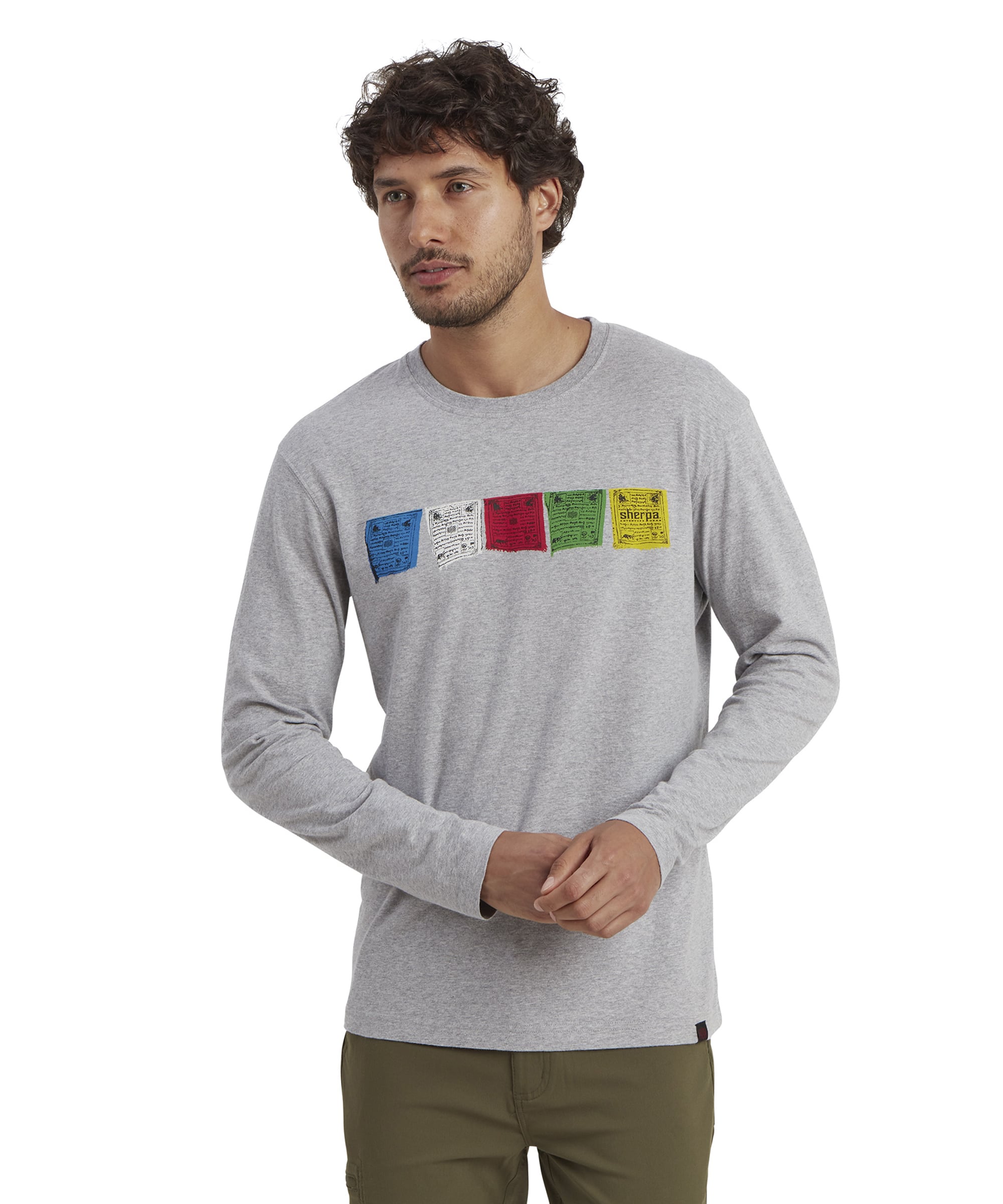 A Sherpa Adventure Gear Tarcho Long Sleeve T-Shirt in Grey featuring a row of colorful prayer flag graphics across the chest in blue, white, red, green, and yellow. The vibrant design symbolizes Tibetan prayer flags and their cultural significance. The model's beard and the upper part of the body are visible, focusing on the details of the shirt's print and texture.