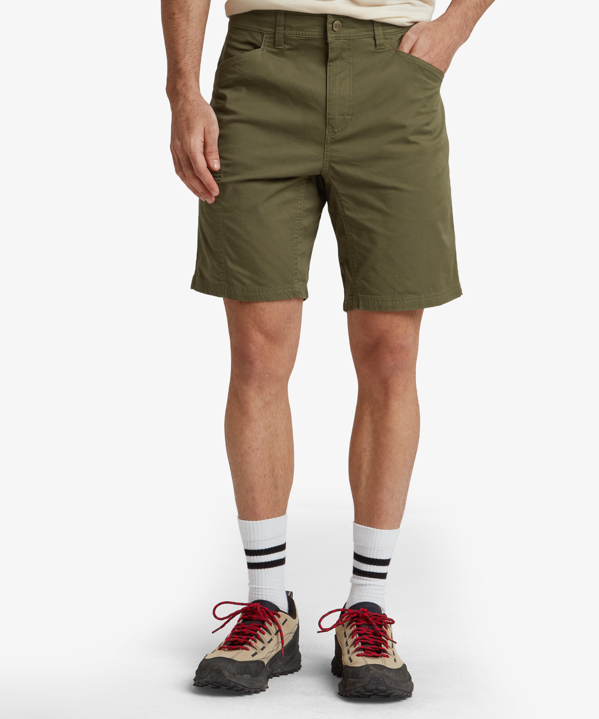 A close-up front view of a pair of Sherpa Adventure Gear Tenjing Shorts in Green with a tailored fit. The shorts feature a zippered pocket on the left thigh and standard hand pockets on both sides. The waistband includes belt loops and is secured by a single button and zipper fly.