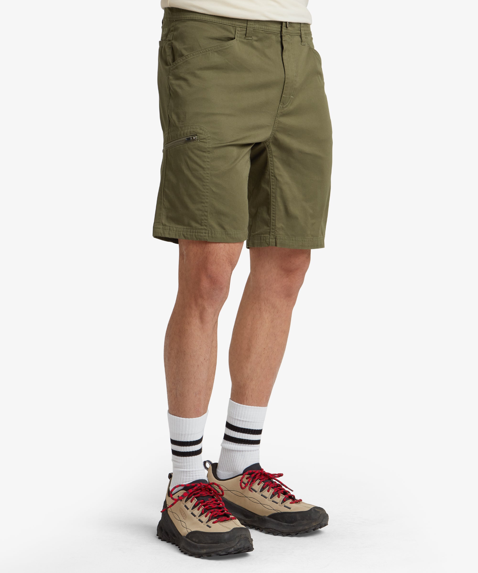 A full back view of the Sherpa Adventure Gear Tenjing Shorts in Green worn by a model, emphasising the structured fit and rear pockets. The shorts include welt pockets on either side, and the fabric appears durable and slightly stretchy. The model is wearing white trainers, adding a casual touch to the outfit.