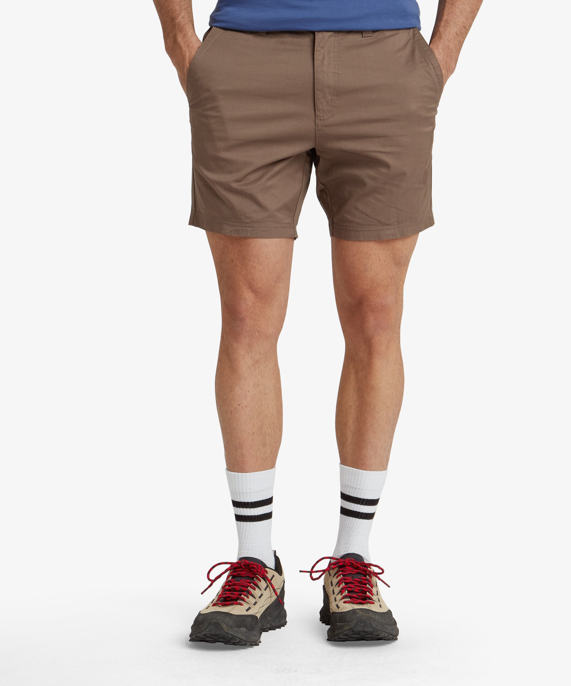 A front view of a model wearing Sherpa Adventure Gear Tenjing Tour Shorts in Grey. The shorts feature a tailored design with a button and zip closure, side pockets, and a clean, classic look. The model pairs the shorts with white trainers, standing against a white background.