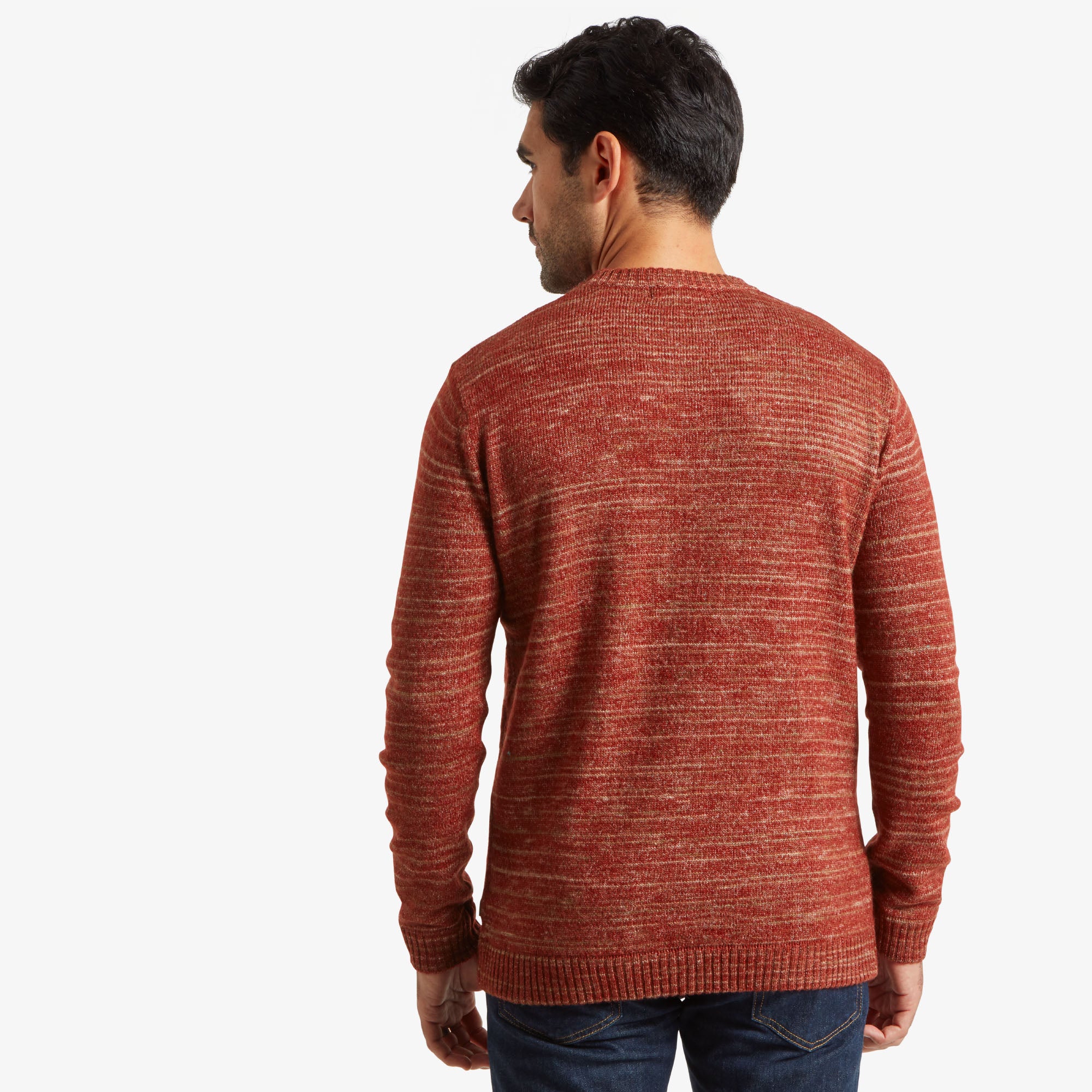 The same man is seen from the back wearing the Sherpa Adventure Gear Vidvan Crew in Brown. The image shows the back of the sweater, highlighting its consistent horizontal marled texture in red and brown hues. The fit is relaxed, with ribbed cuffs and a hem. The neckline sits comfortably at the base of his neck. The man's dark hair is visible, and he is standing with his hands at his sides.