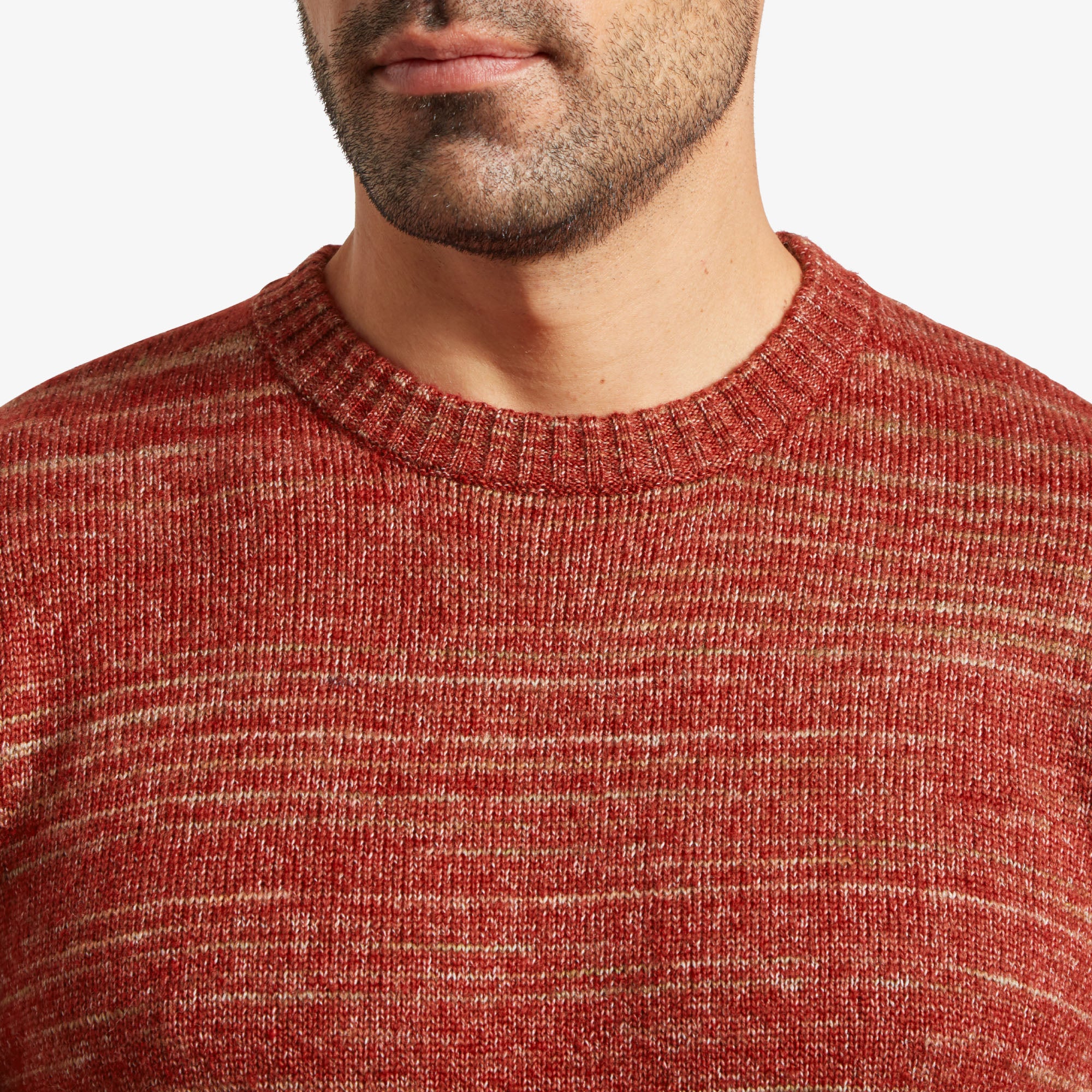 A close-up of the upper part of the Sherpa Adventure Gear Vidvan Crew in Brown, focusing on the crew neckline and knit texture. The marled design combines red and subtle lighter brown tones, creating a visually textured effect. The ribbed collar fits snugly around the man's neck, and his jawline and slight beard are partially visible. The texture of the sweater appears soft and cozy.