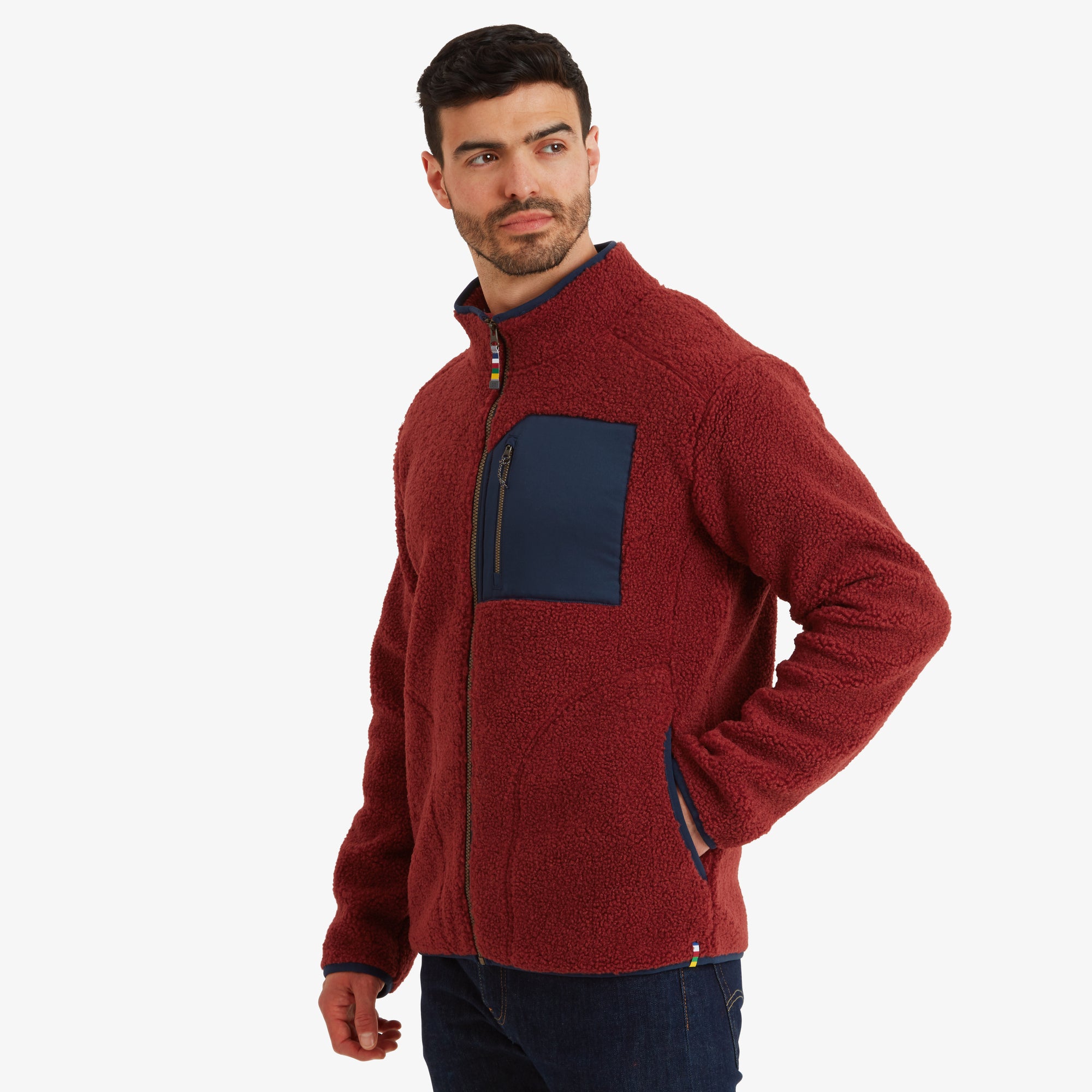 The model is turned slightly to the side, showing the fit of the Sherpa Adventure Gear Yatri Full Zip Jacket in Light Brown's shoulders and sleeves. The navy chest pocket and side hand pockets with navy trim are visible, emphasising the practical design details.