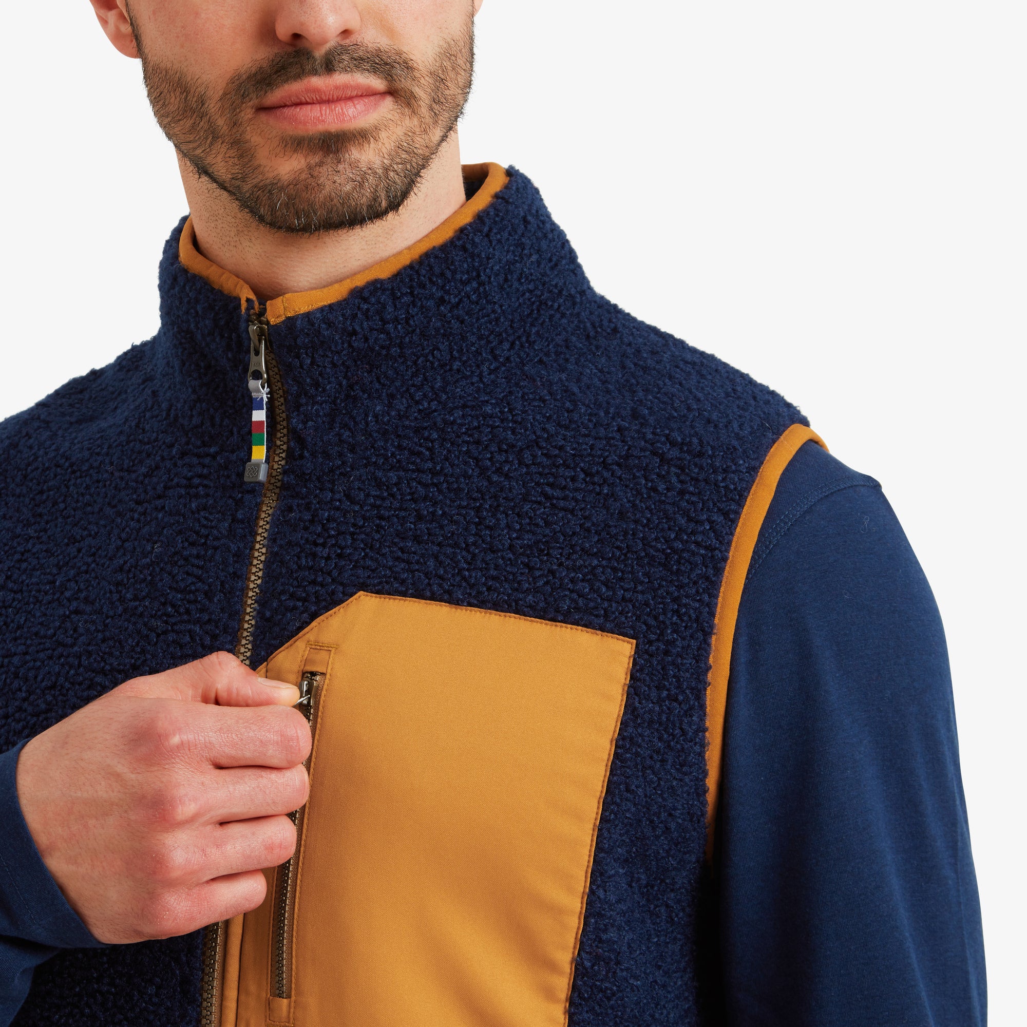 Close-up of the chest pocket and zipper details. The mustard yellow chest pocket with a zipper is prominently displayed, with the Sherpa Adventure Gear Yatri Vest in Blue’s textured navy blue fabric and orange accents offering a stylish contrast.