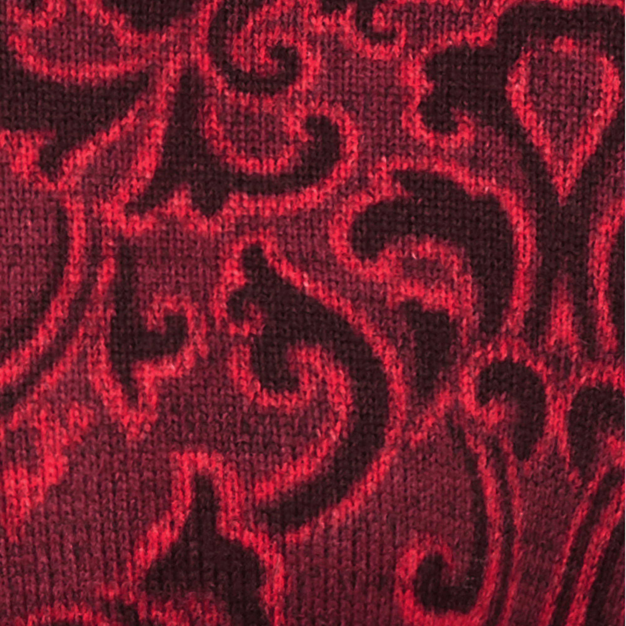 Close-up view of the fabric pattern from a Sherpa Adventure Gear Namla Hooded Jacket II in Red. The fabric features a vibrant red base with intricate swirling paisley-like designs in a deeper shade of red. The knit texture is clearly visible, highlighting the fine details of the pattern and the slightly raised design elements.