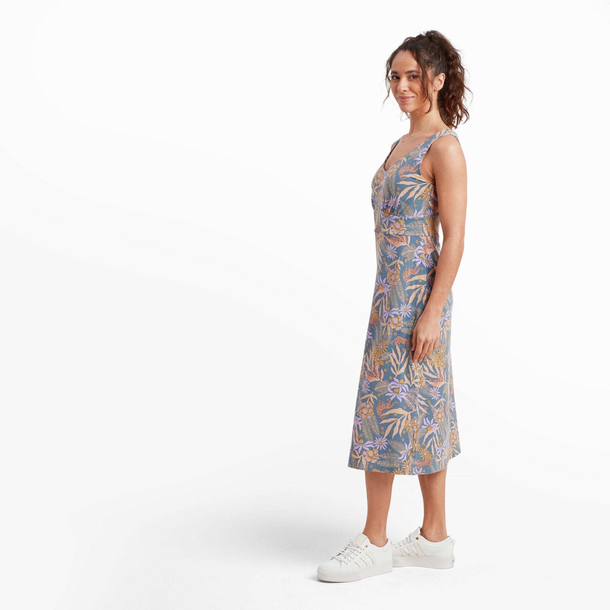 The model is seen in profile, showcasing the clean lines of the Sherpa Adventure Gear Neha Midi Dress in Blue and its tailored fit around the waist. The light, flowing fabric of the midi dress enhances its elegant yet relaxed aesthetic.