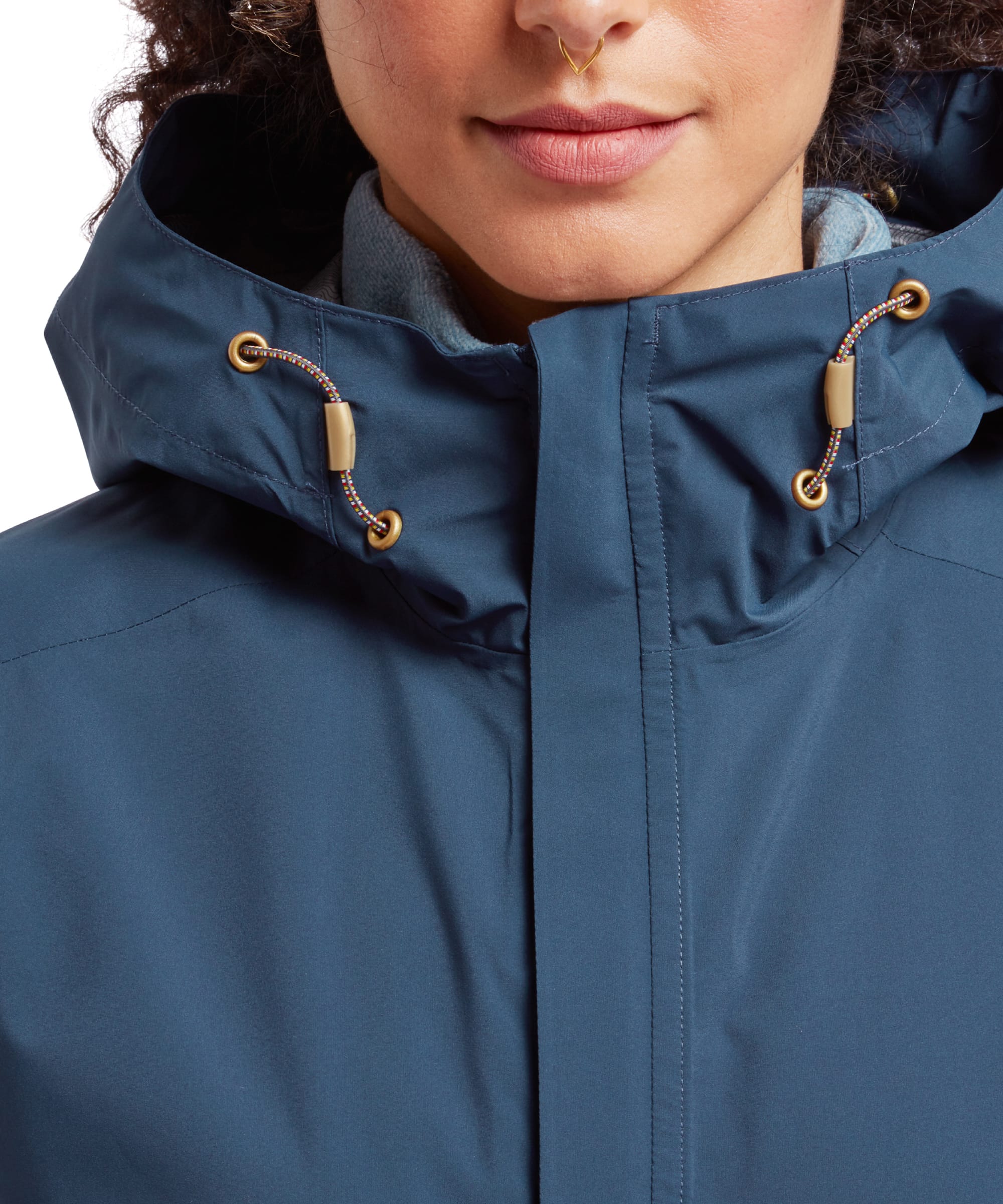 A zoomed-in view of the left side of the Sherpa Adventure Gear Nima 2.5-Layer Jacket in Blue, featuring a hand in the pocket. The Sherpa logo is embroidered in contrasting beige near the hem, and the cuff shows a Velcro adjustment tab.