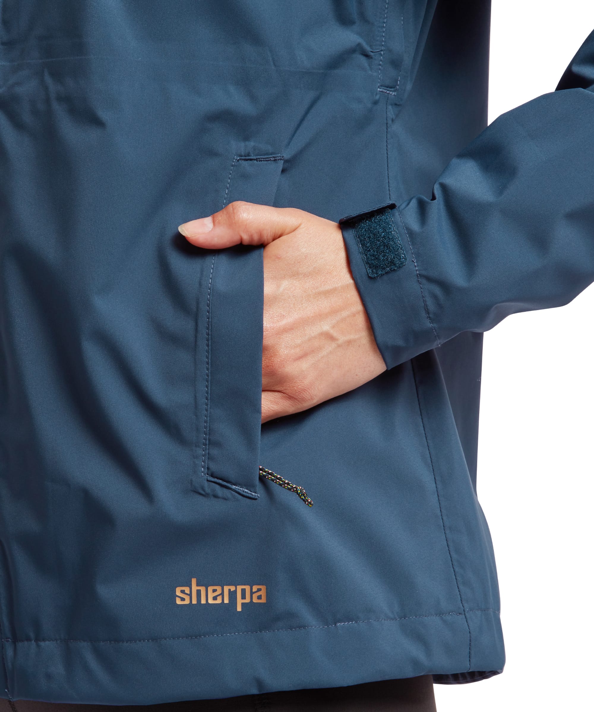 A detailed shot of the Sherpa Adventure Gear Nima 2.5-Layer Jacket in Blue's hood, showing its adjustable drawstrings with beige toggles. The model's face is partially visible, highlighting her lips and curly hair framing her face.