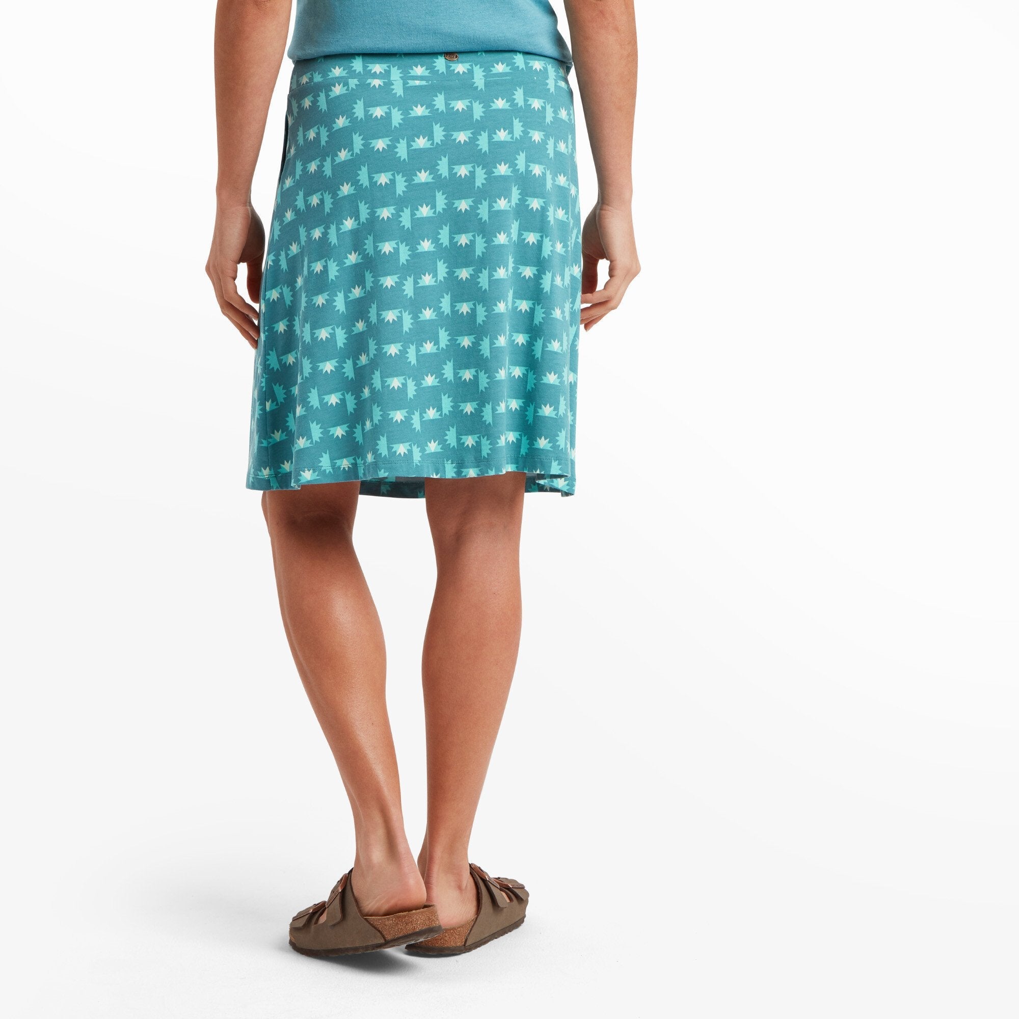 Rear view of the woman modeling the Sherpa Adventure Gear Padma Pull On Skirt in Blue, showing the back fit. The waistband sits smoothly at her natural waist, and the skirt falls in a gentle flare to just above her knees. The all-over print is consistent, and her sandals are visible from behind.