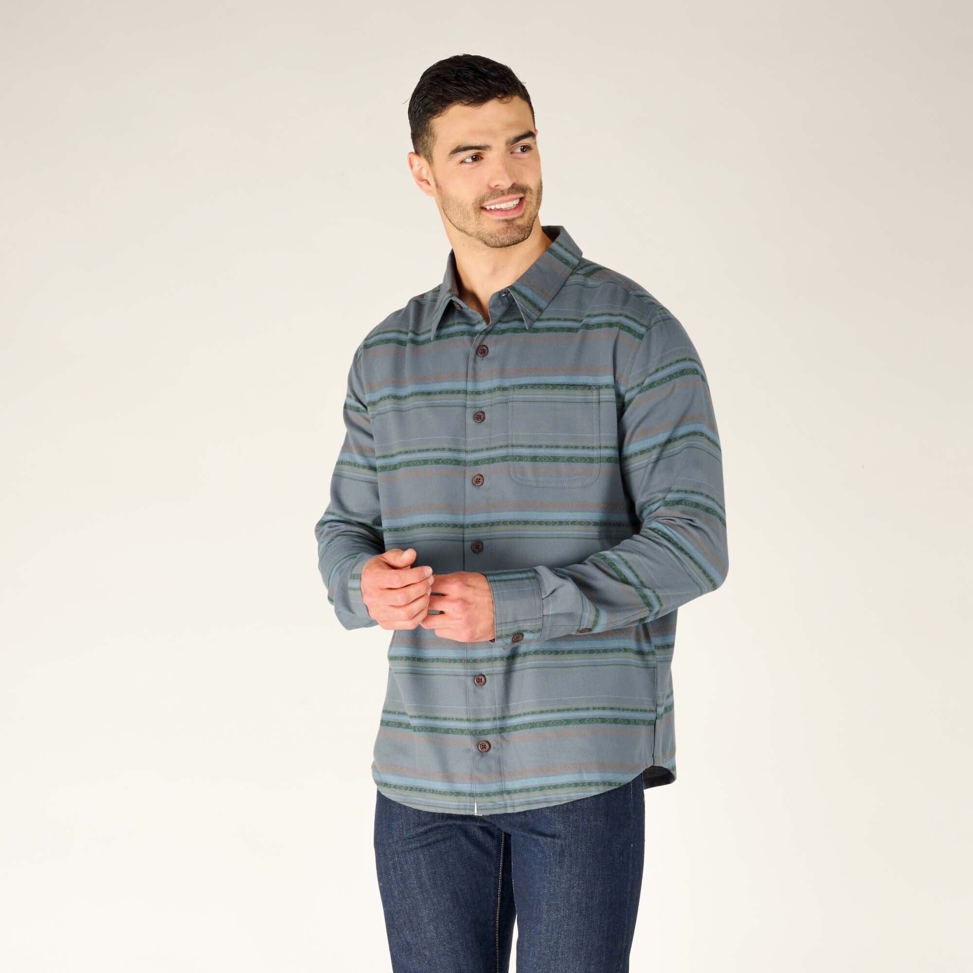 The model is facing slightly to the left, with his arms relaxed at his sides. The detailing of the Sherpa Adventure Gear Pasang Shirt in Blue's buttons and subtle striped patterns is more visible, emphasising its casual yet polished design.