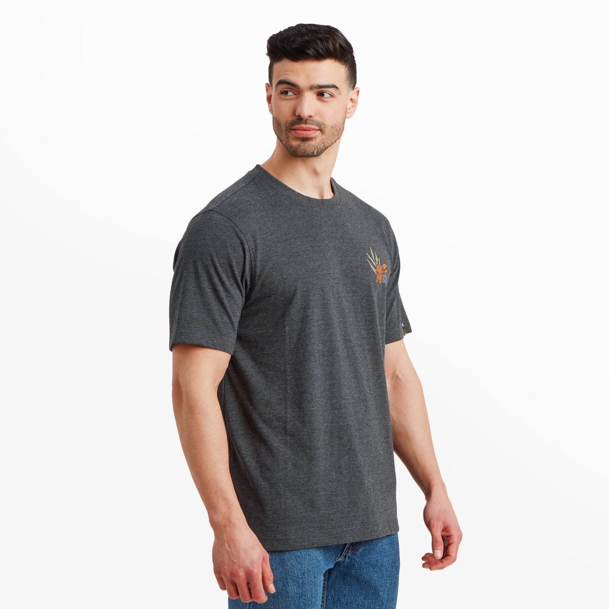 The same male model turned slightly to his right, showcasing the side profile of the Sherpa Adventure Gear Purpose T-Shirt in Black. The fit is relaxed, and the graphic on the left chest remains partially visible, while the sleeves have a clean, simple cut.