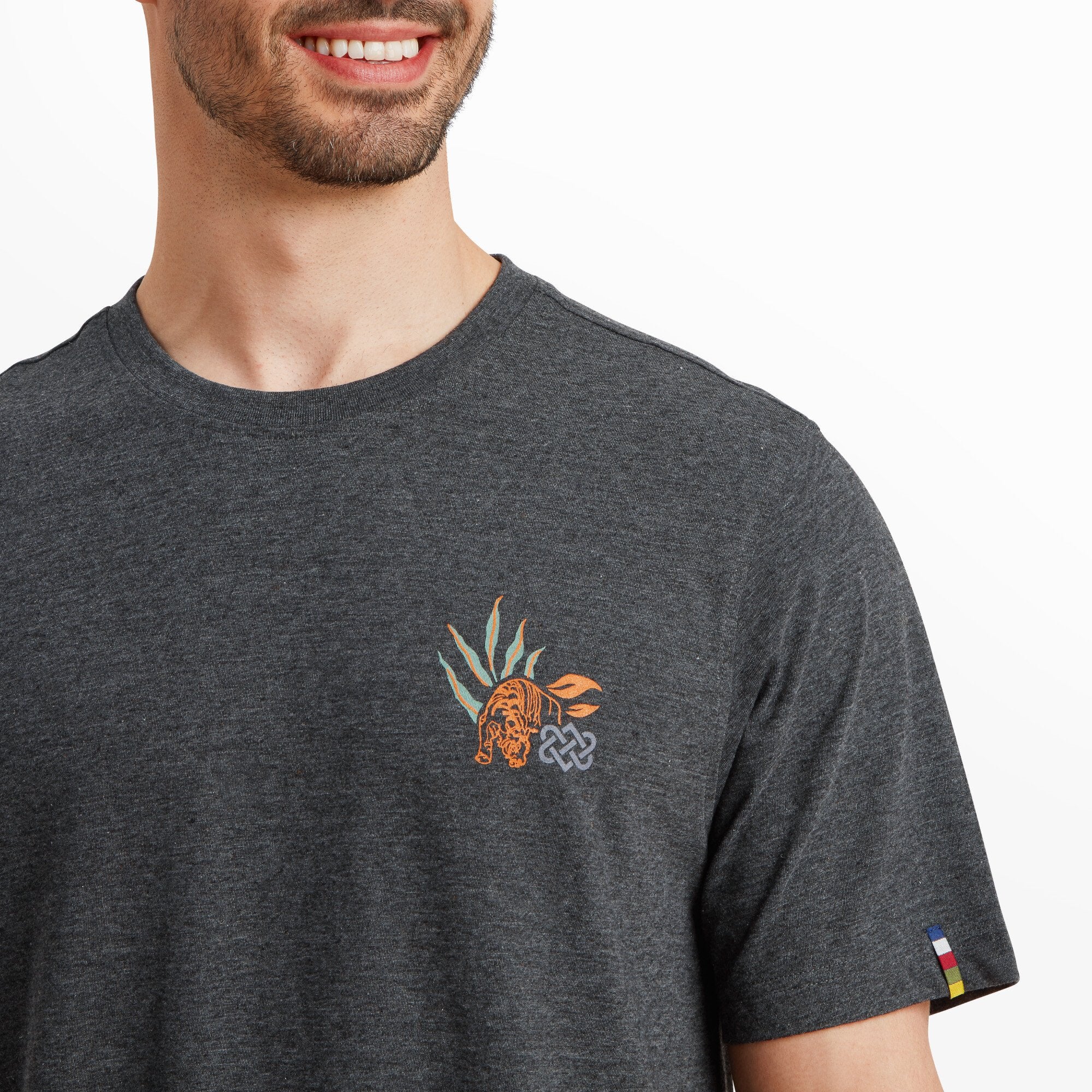 A close-up shot of the left chest area of the Sherpa Adventure Gear Purpose T-Shirt in Black, emphasising the detailed tiger graphic surrounded by stylized green and orange leaves. The intricate print adds a pop of color to the dark gray fabric.