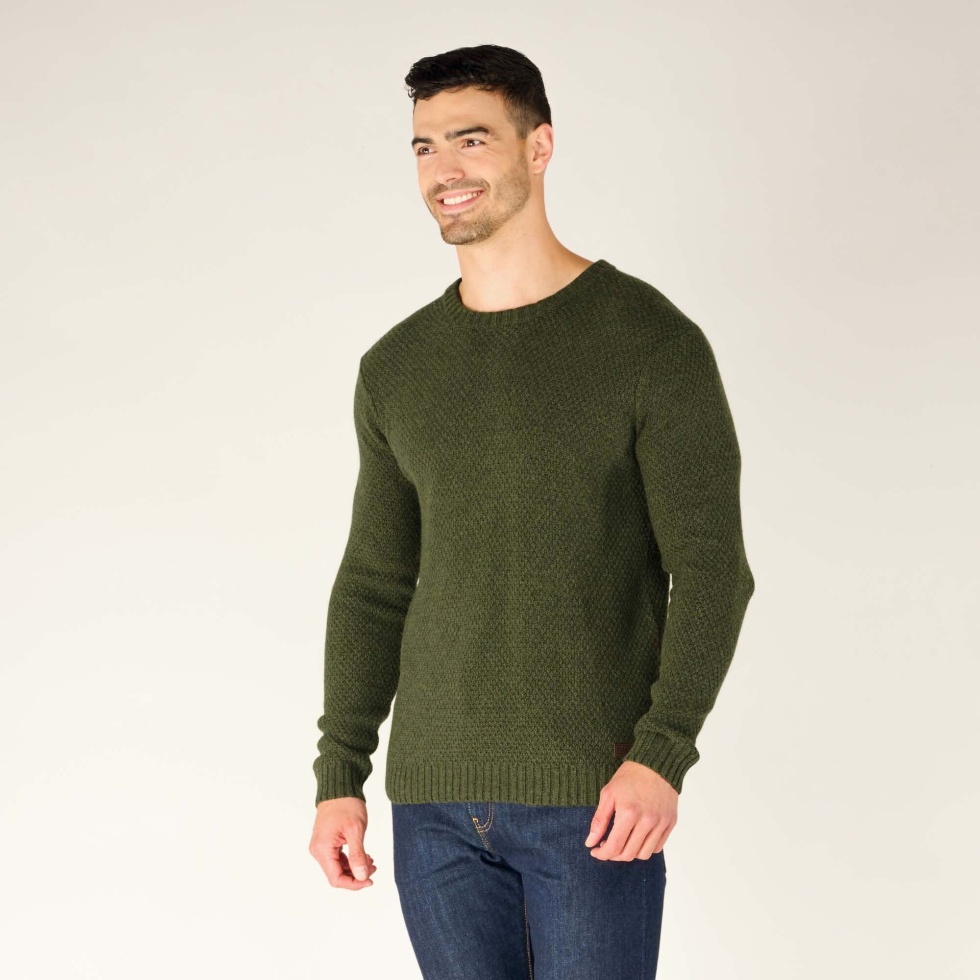 The model stands in a relaxed pose, turned slightly to his right, showcasing the side profile of the green textured crewneck sweater. The textured knit pattern is clearly visible, and the ribbed cuffs and hem keep the sweater comfortably in place. His hands hang at his sides.